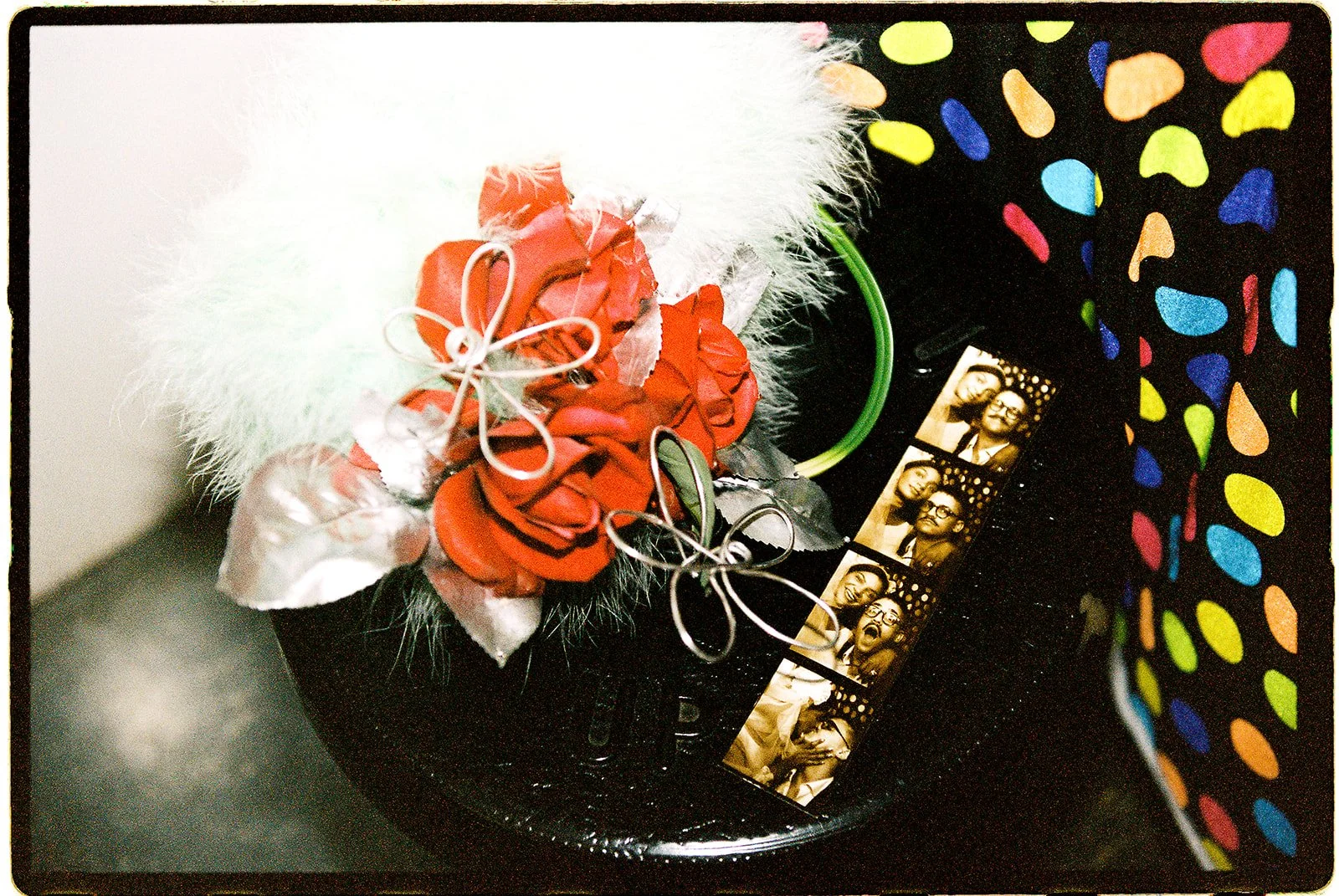 Black-and-white wedding photostrips beside a red rose bouquet with white feathers and silver ribbon details.