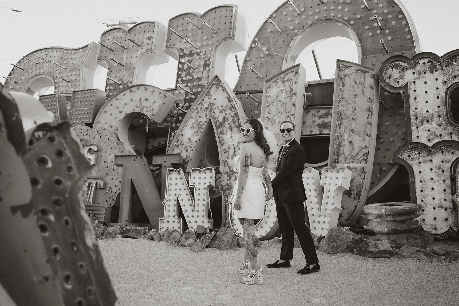 Black and white photo of the bride and groom holding hands while walking through the Neon Museum North Gallery.