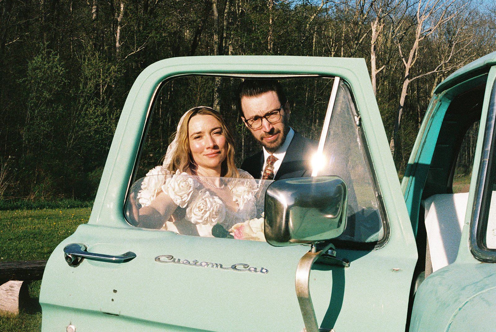 Bride and groom posing behind the window of a vintage green truck.