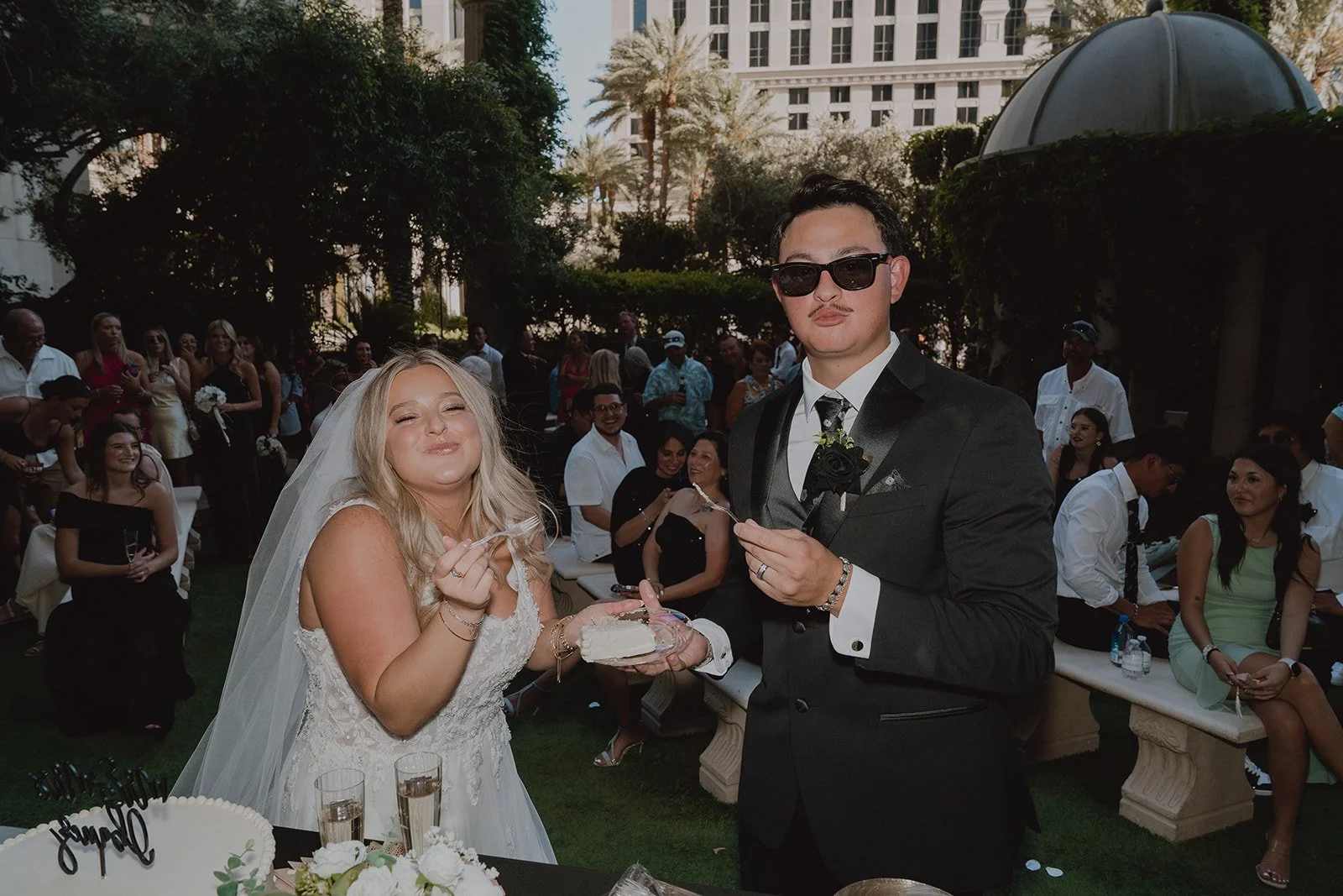 Bride and groom feeding each other cake in the Venus Garden at Caesars Palace surrounded by guests.
