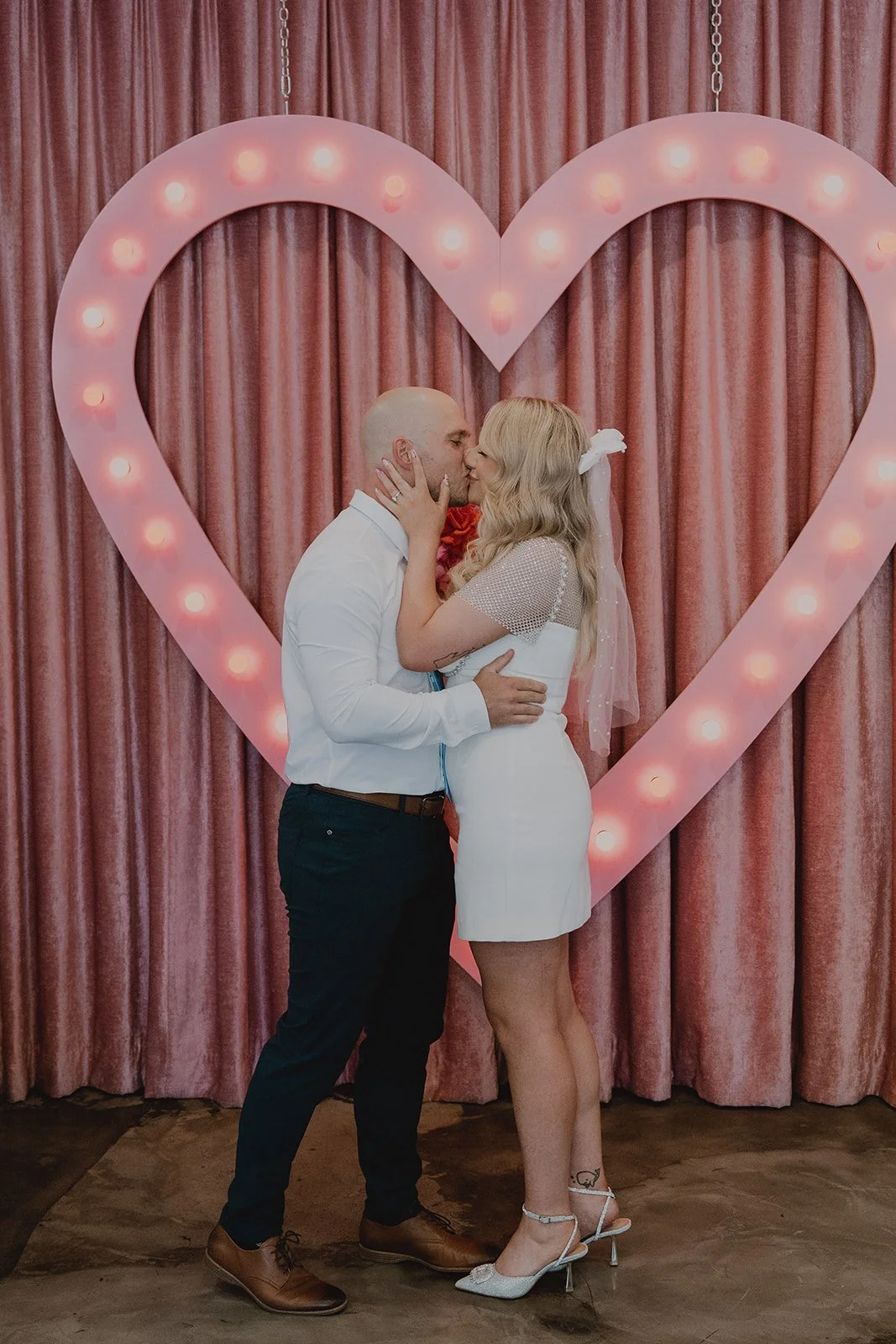 First kiss beneath the pink heart backdrop at a Sure Thing Chapel Las Vegas micro wedding.