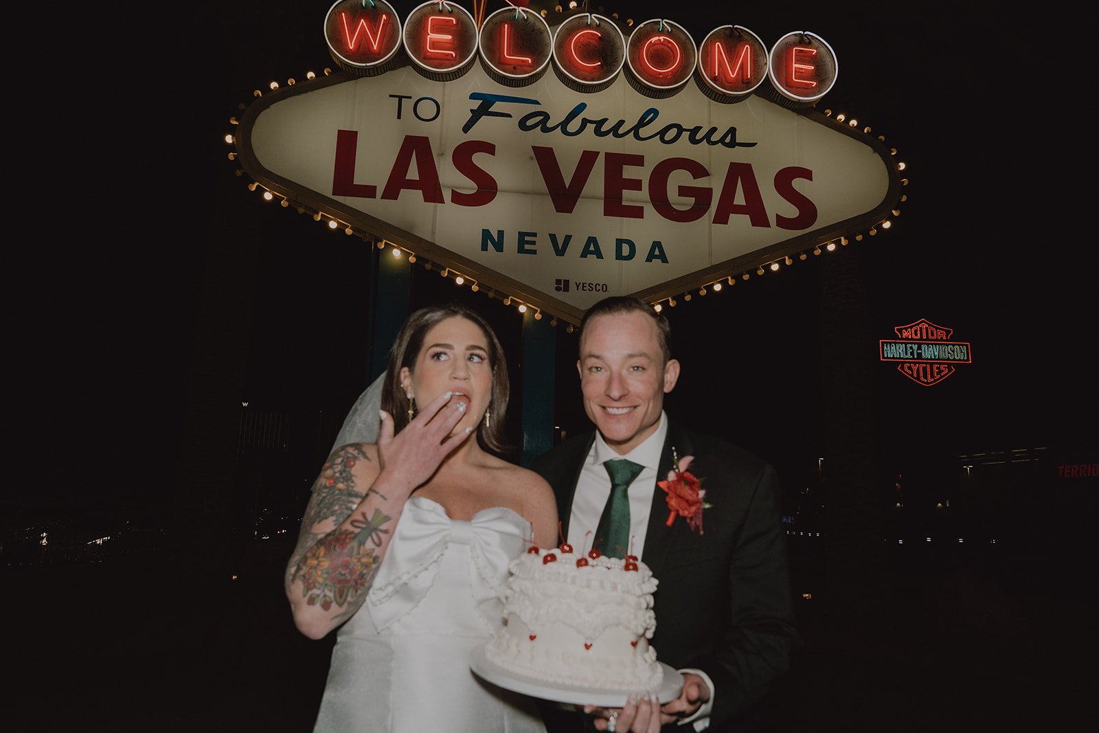 Bride eating frosting in front of the Welcome to Fabulous Las Vegas sign during nighttime wedding photos.