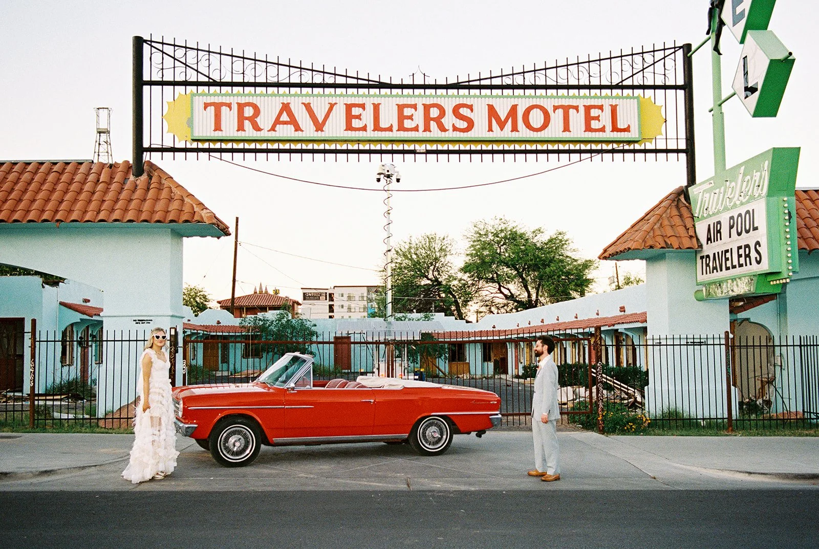 Wide shot of a couple posing with the red convertible outside of Sure Thing Chapel in Las Vegas.