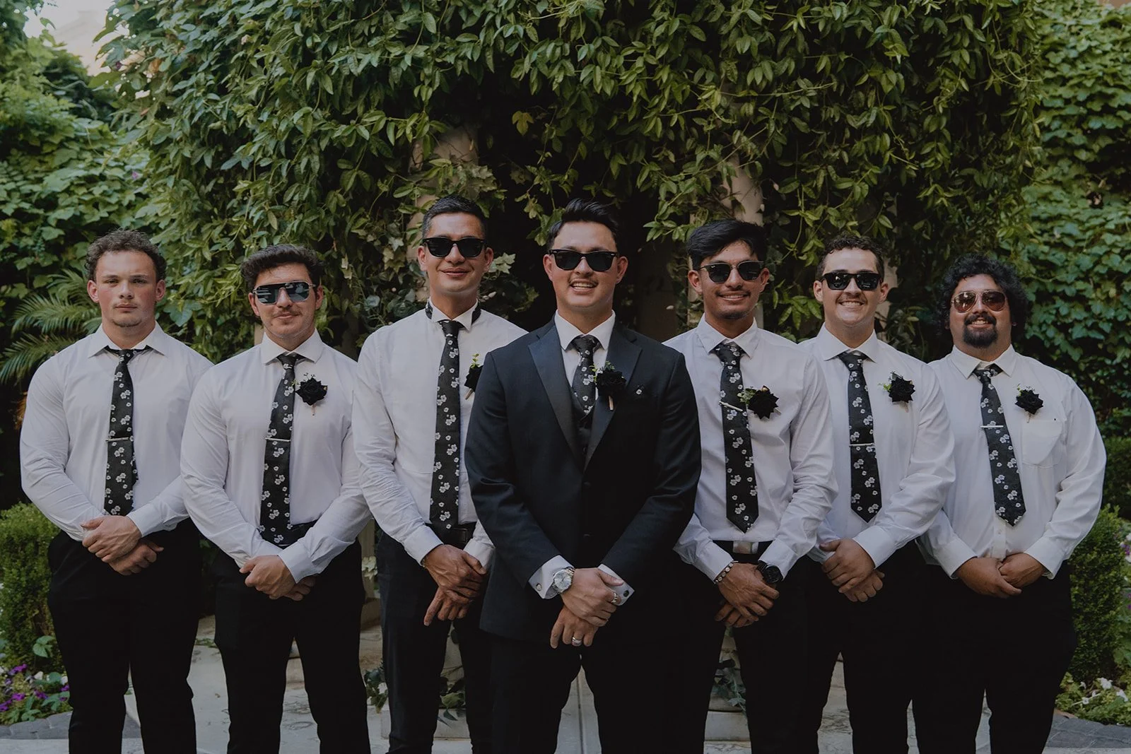 Groom standing with groomsmen wearing white shirts, black ties, and black pants during a Caesars Palace Venus Garden wedding.