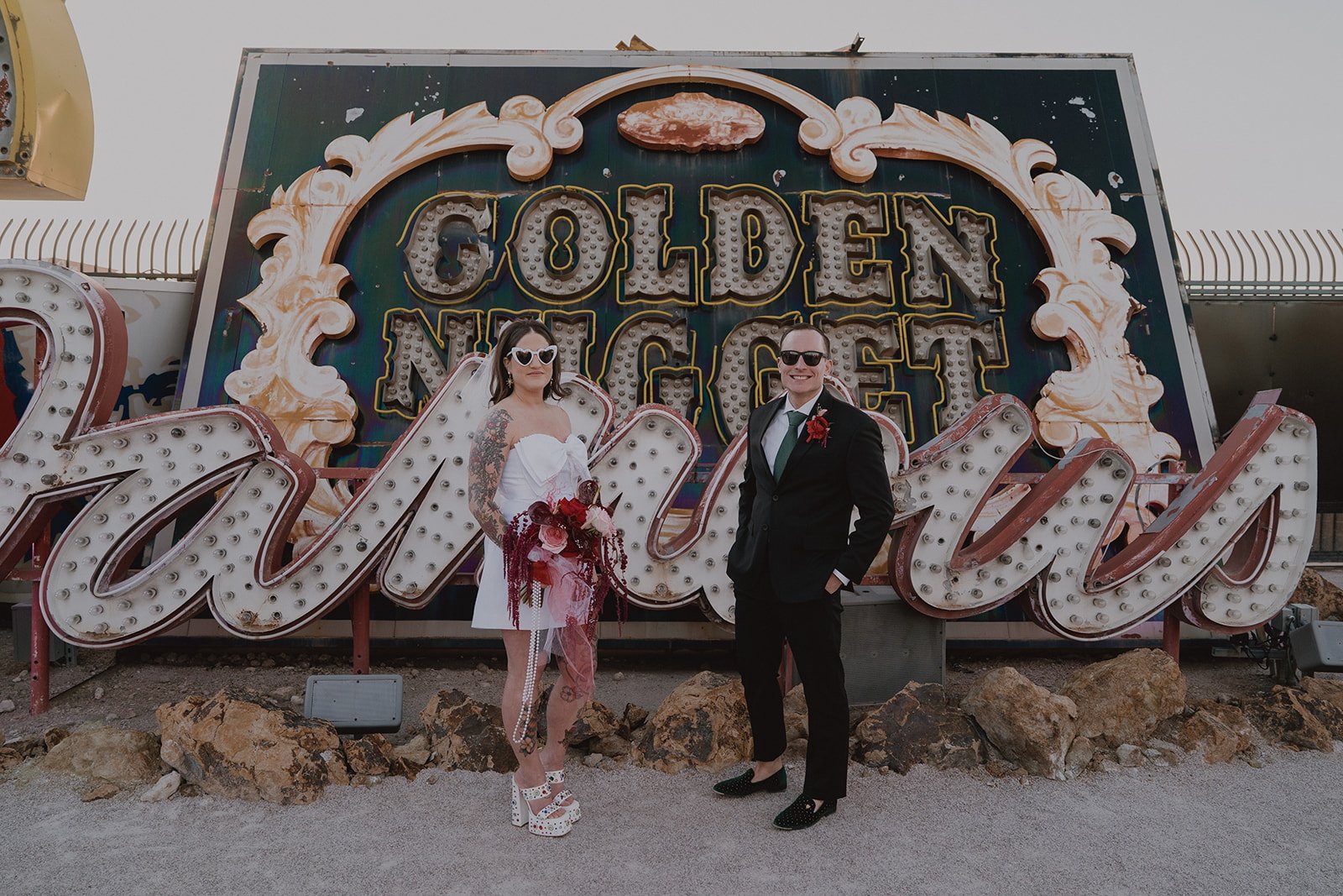 Bride and groom posing together in front of layered vintage signage in the Neon Museum North Gallery.
