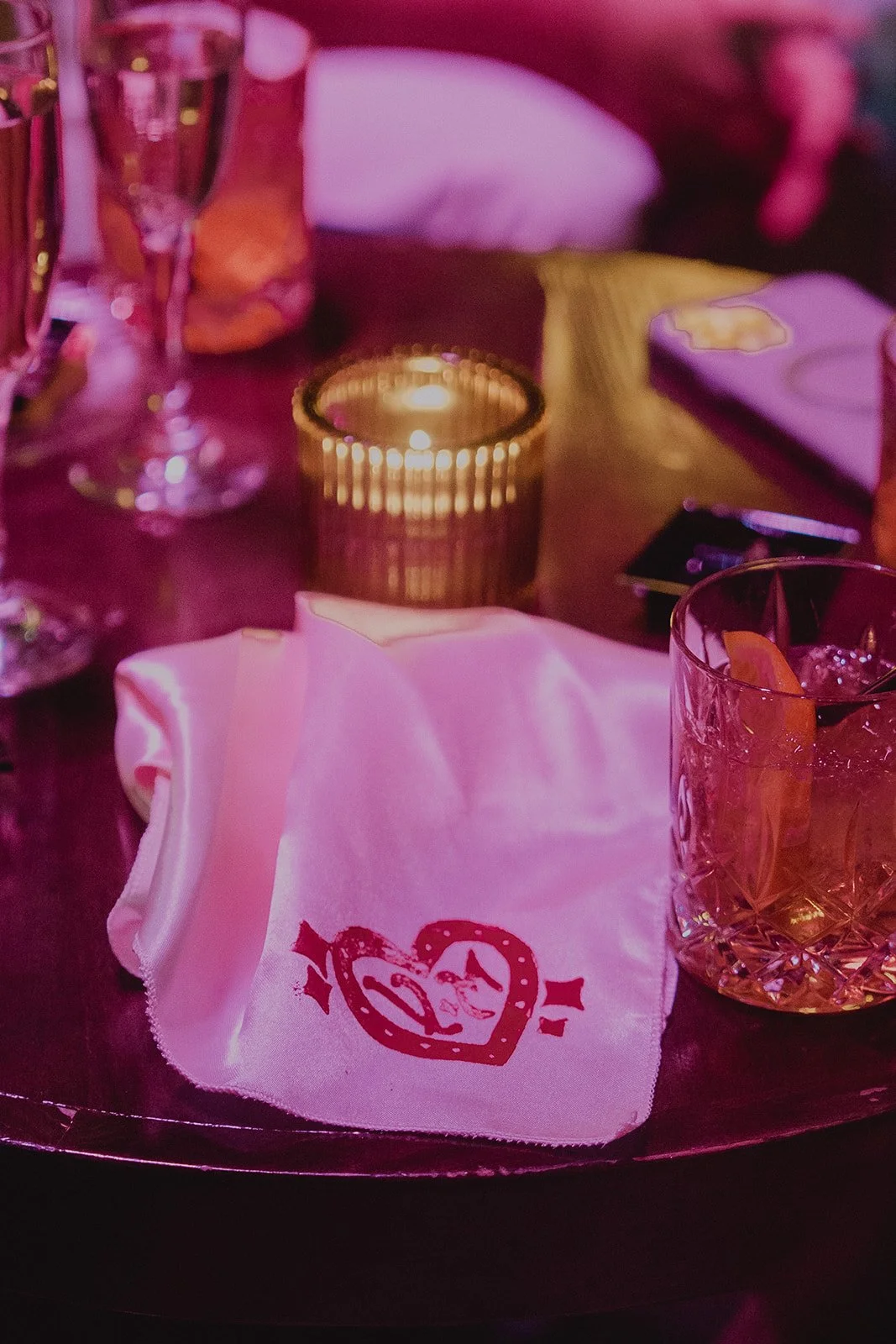 Wedding reception details with a handkerchief, candle, and cocktail under pink lighting.