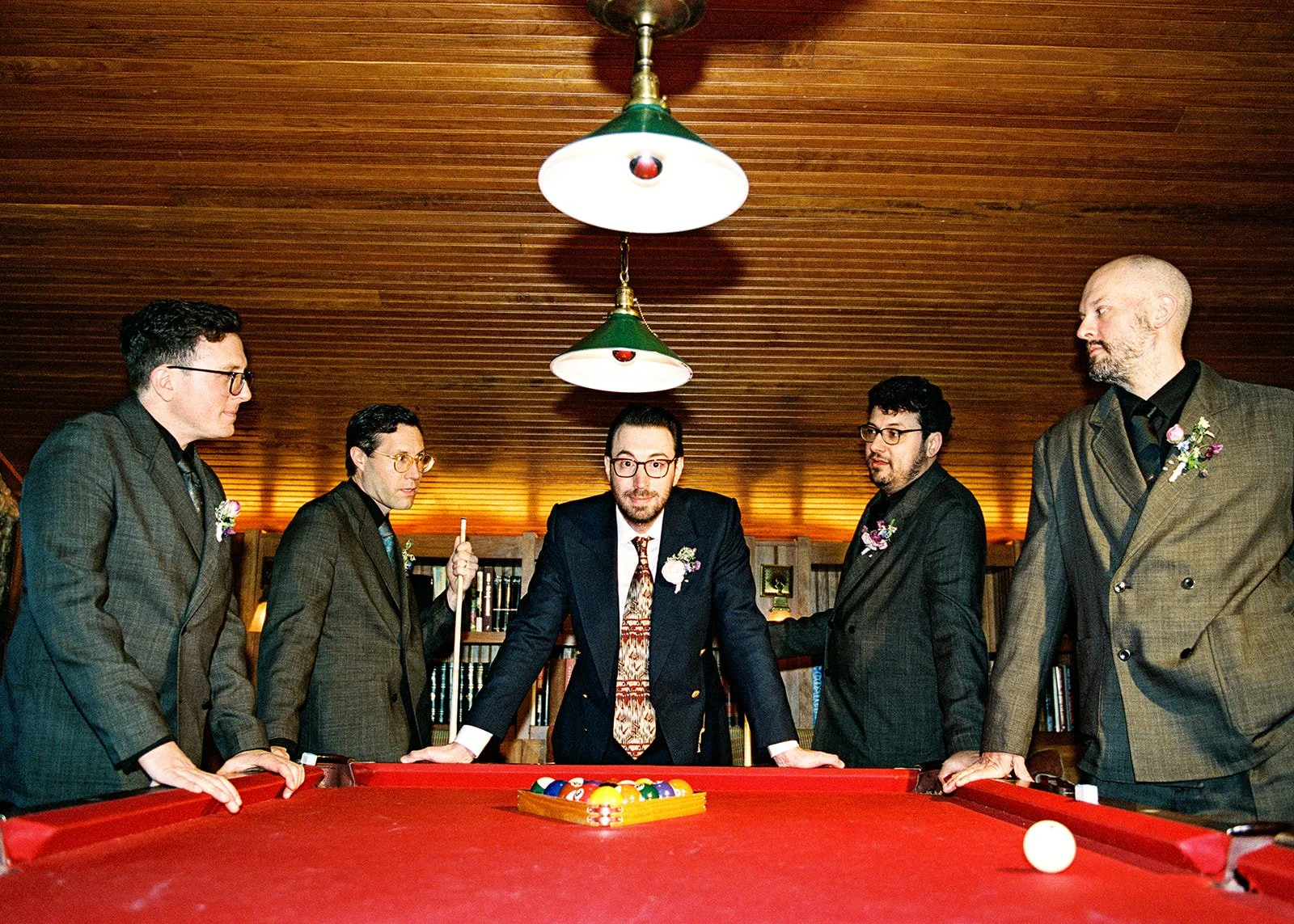 Film wedding party photo of the groom and groomsmen gathered around the red pool table inside the Deer Mountain Inn Attic.