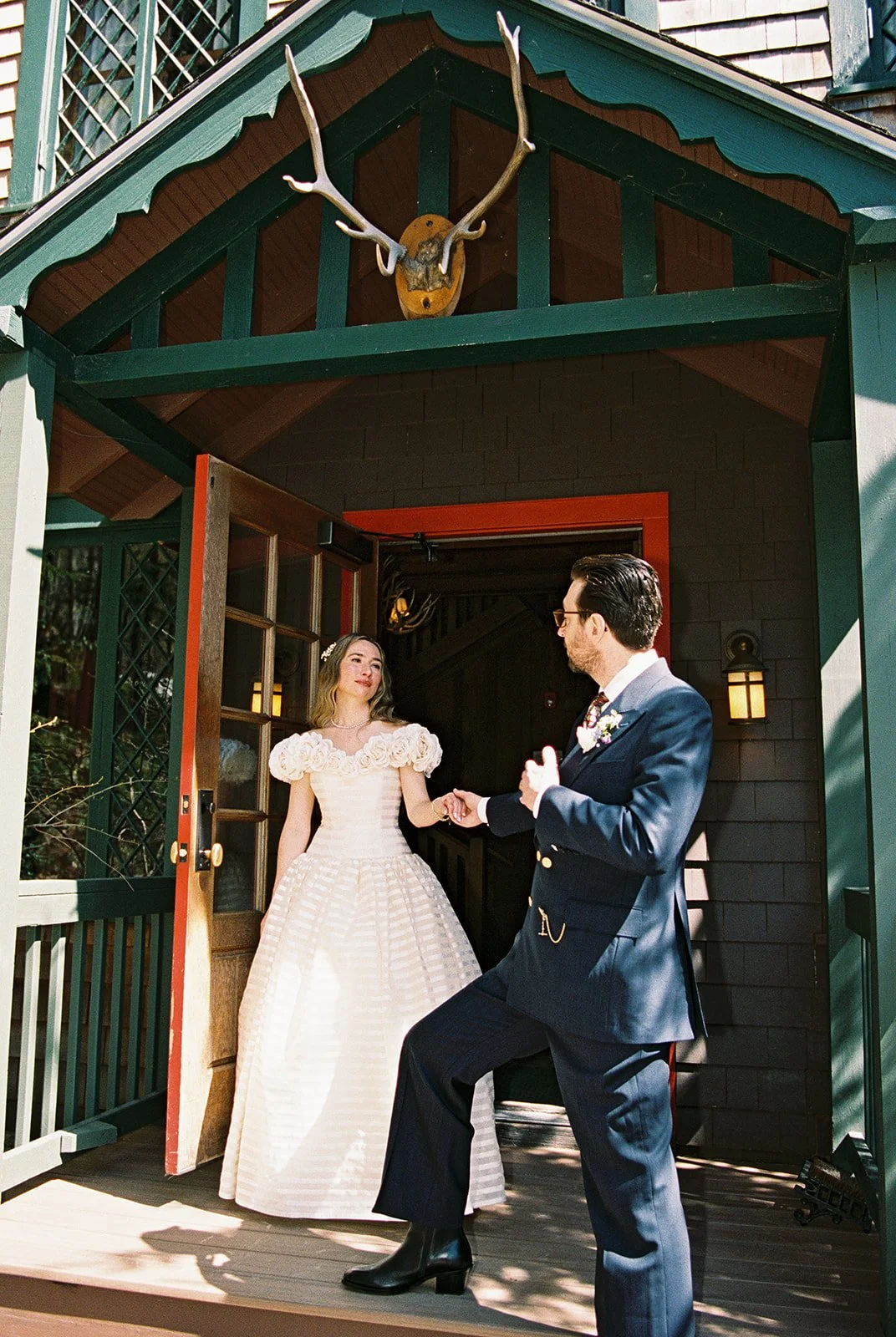 Playful film photo of the bride and groom holding hands outside the rustic entrance of Deer Mountain Inn.