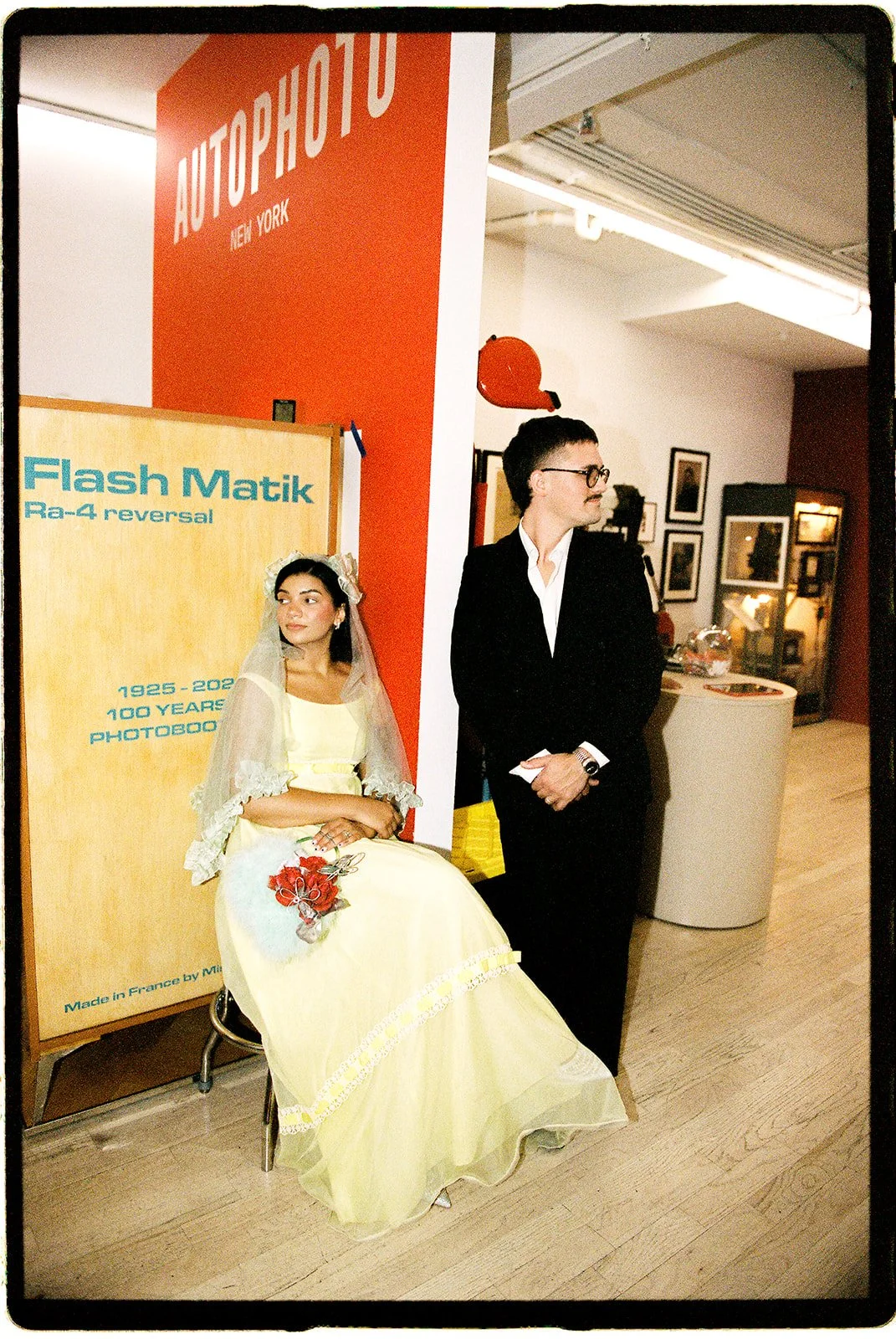 Newlyweds posing beside a vintage photobooth display inside the AUTOPHOTO Museum in New York City.