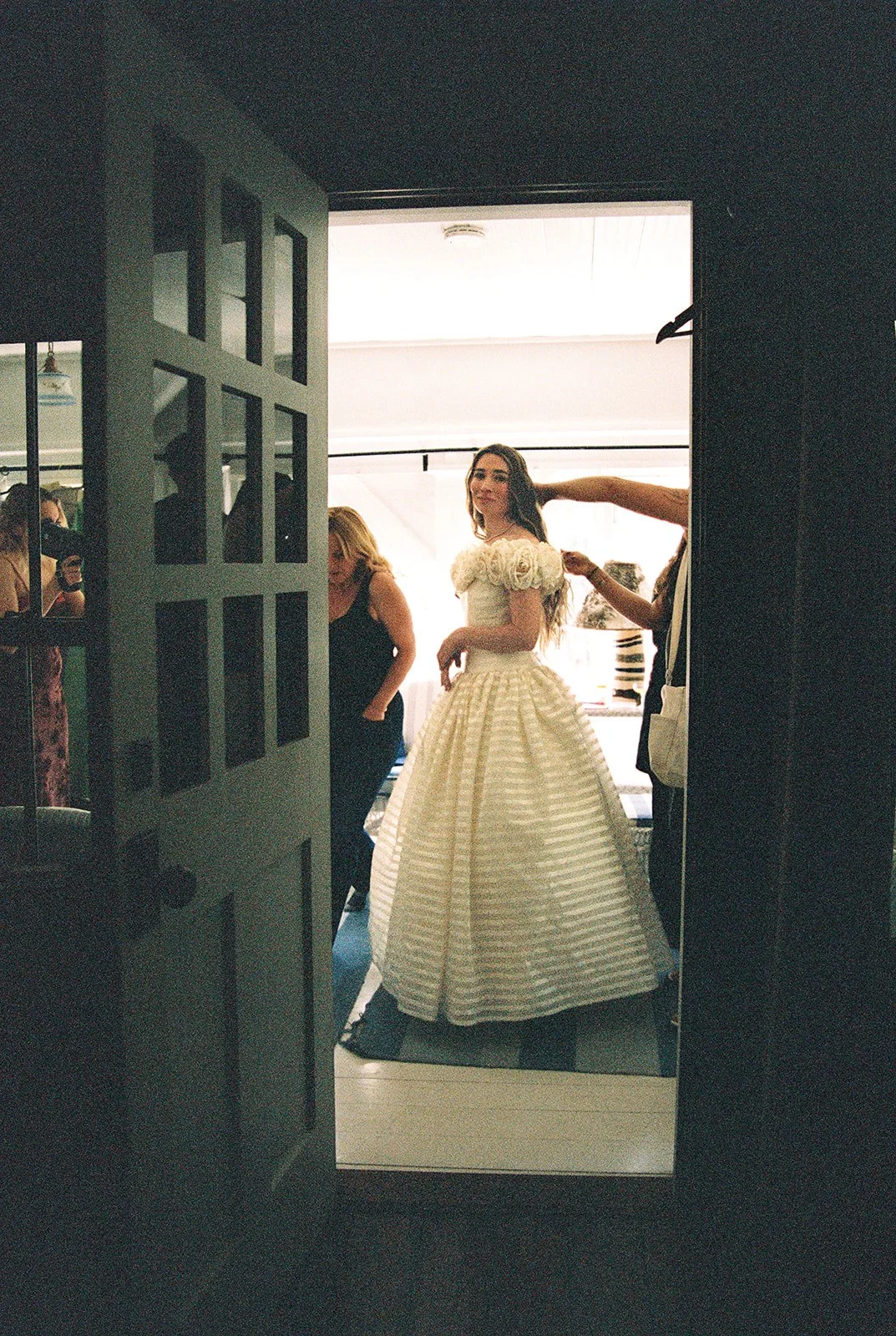 Film photo of the bride framed through a doorway while her wedding party helps with her dress inside the Tuckaway cottage.