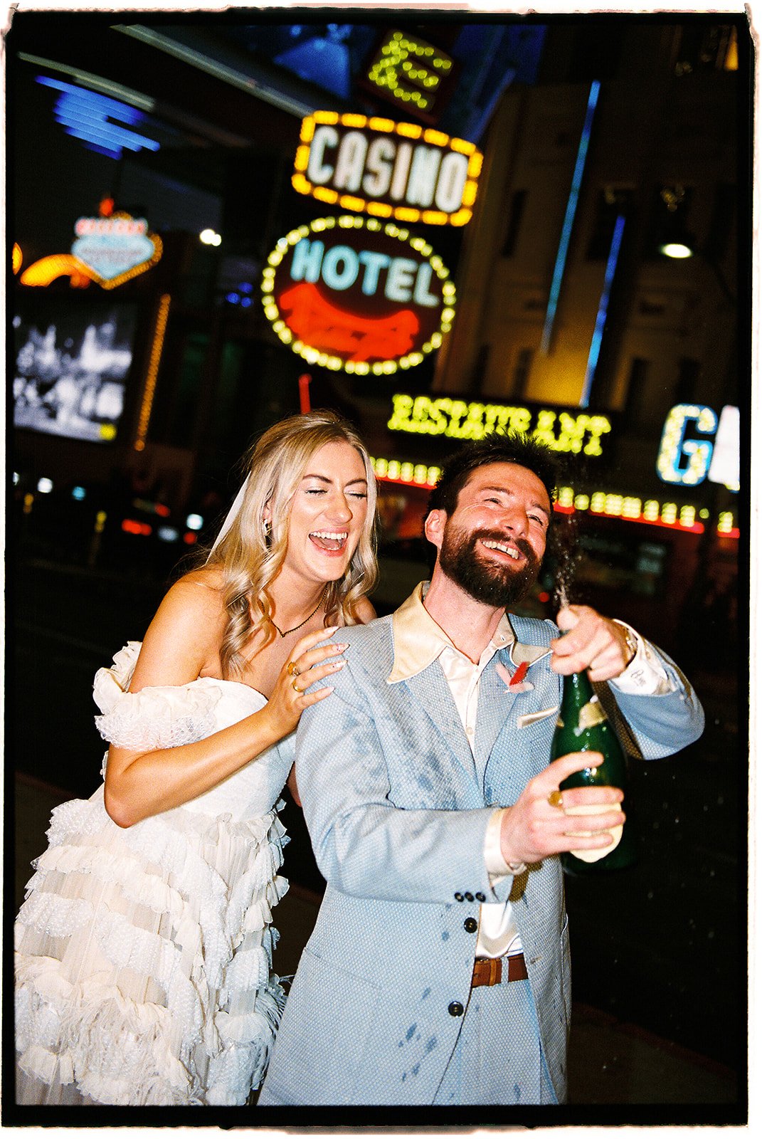 35mm film photo of a bride and groom popping champagne on Fremont Street in front of Golden Gate Casino & Hotel.
