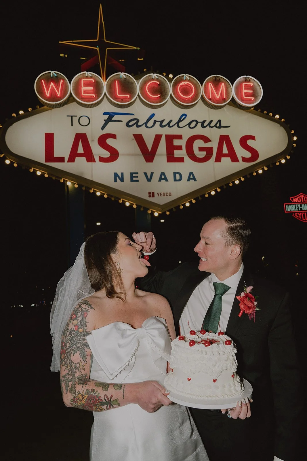 Groom feeding the bride cherries during Welcome to Fabulous Las Vegas sign wedding photos at night.