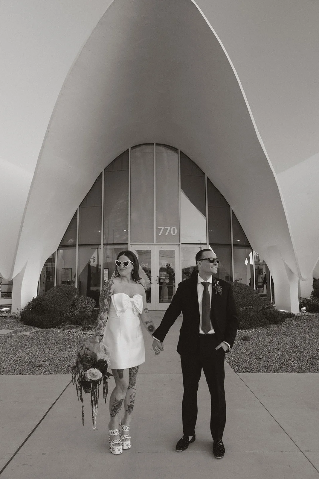 Black and white photo of a bride and groom posing outside of The Neon Museum in Las Vegas.