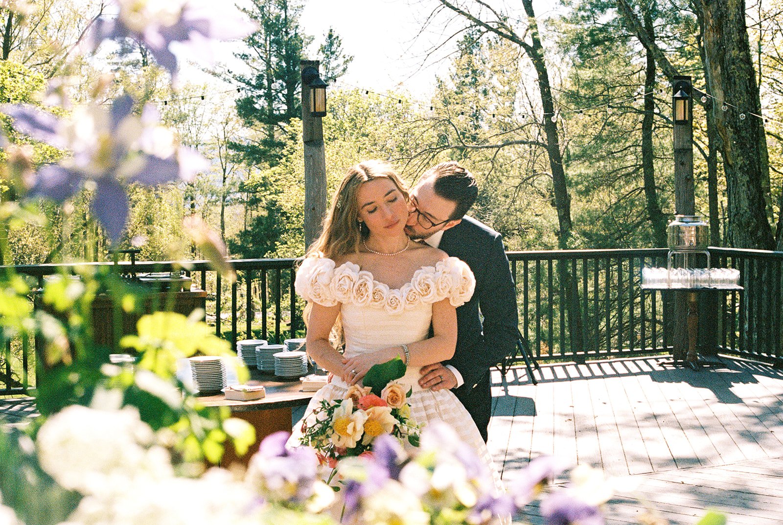 Film photo of the groom kissing the bride’s cheek as she holds a colorful bouquet on the terrace at Deer Mountain Inn.