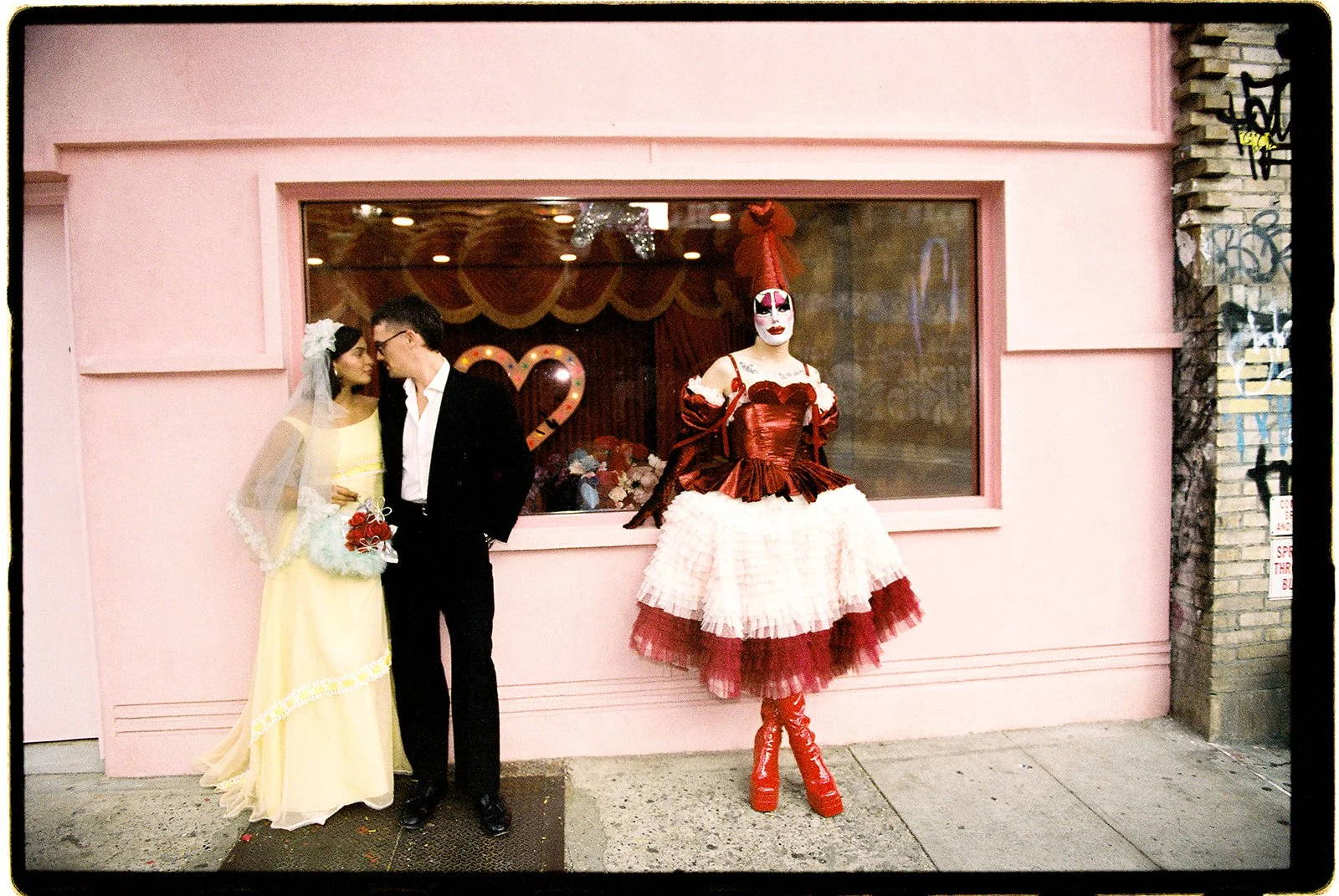 Newlyweds standing outside the pink Sure Thing NYC wedding chapel with Tillie the Clown in a red and white costume.