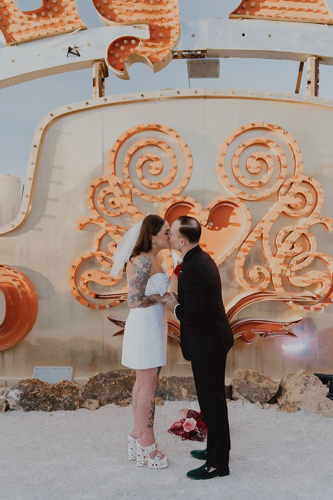 Bride and groom kissing in front of glowing vintage signage at the Neon Museum during golden hour.