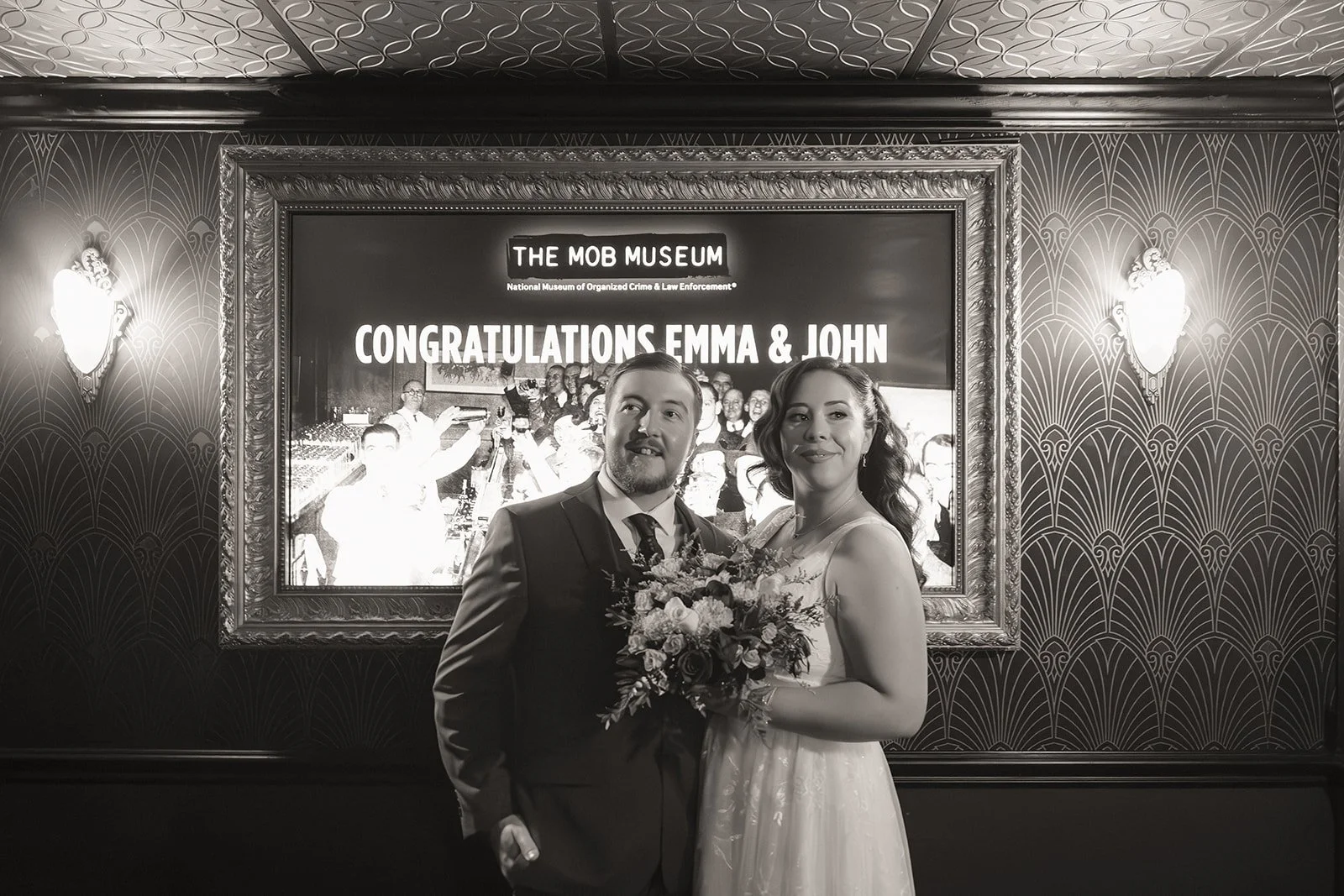 Black and white photo of a bride and groom poising in front of a sign at The Mob Museum in Las Vegas.