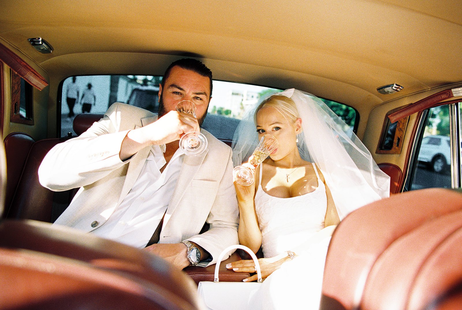 Bride and groom drinking champagne inside a classic car from Royal Rides.