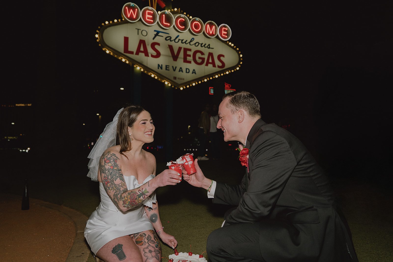 Bride and groom clinking their red solo cups filled with wedding cake in front of the Welcome to Fabulous Las Vegas sign.