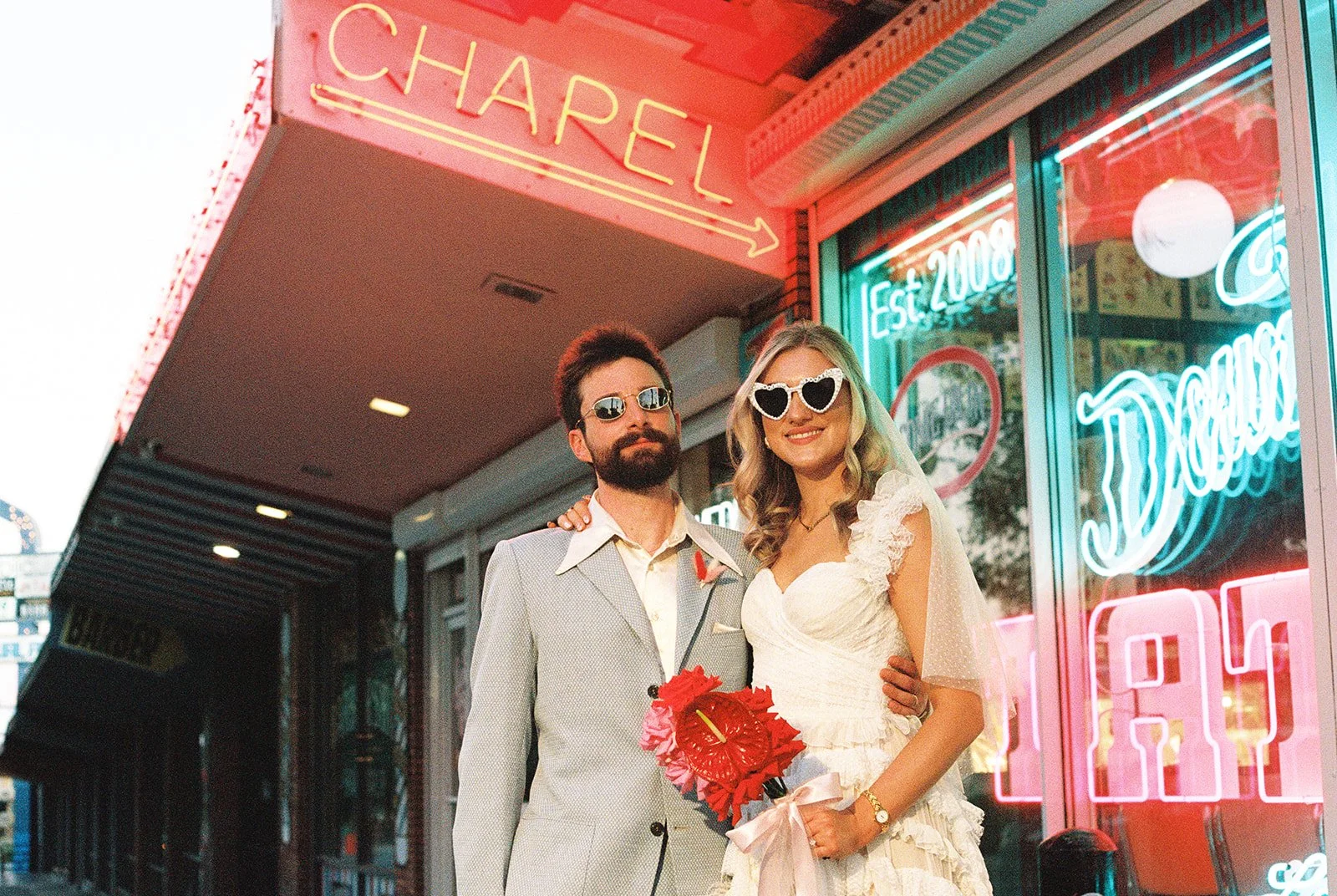 Bride and groom posing in front of Sure Thing Chapel in Las Vegas wearing sunglasses.