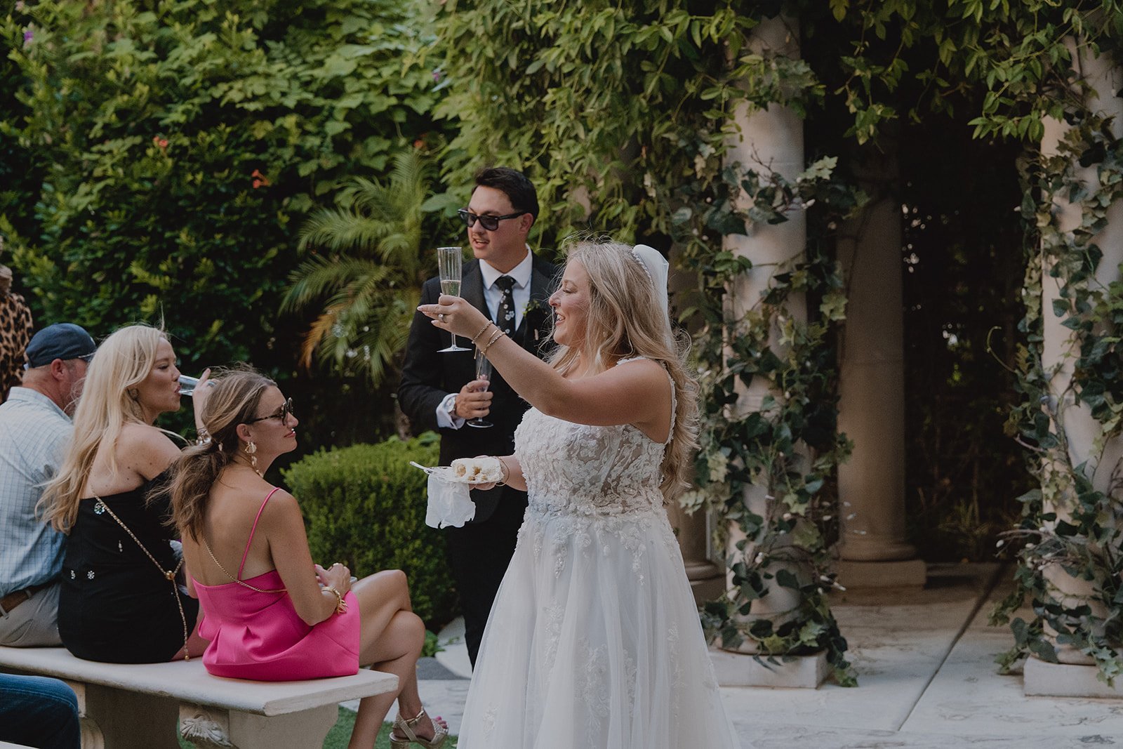 Bride and groom holding cake plates and champagne while guests watch during a Caesars Palace Venus Garden wedding celebration.