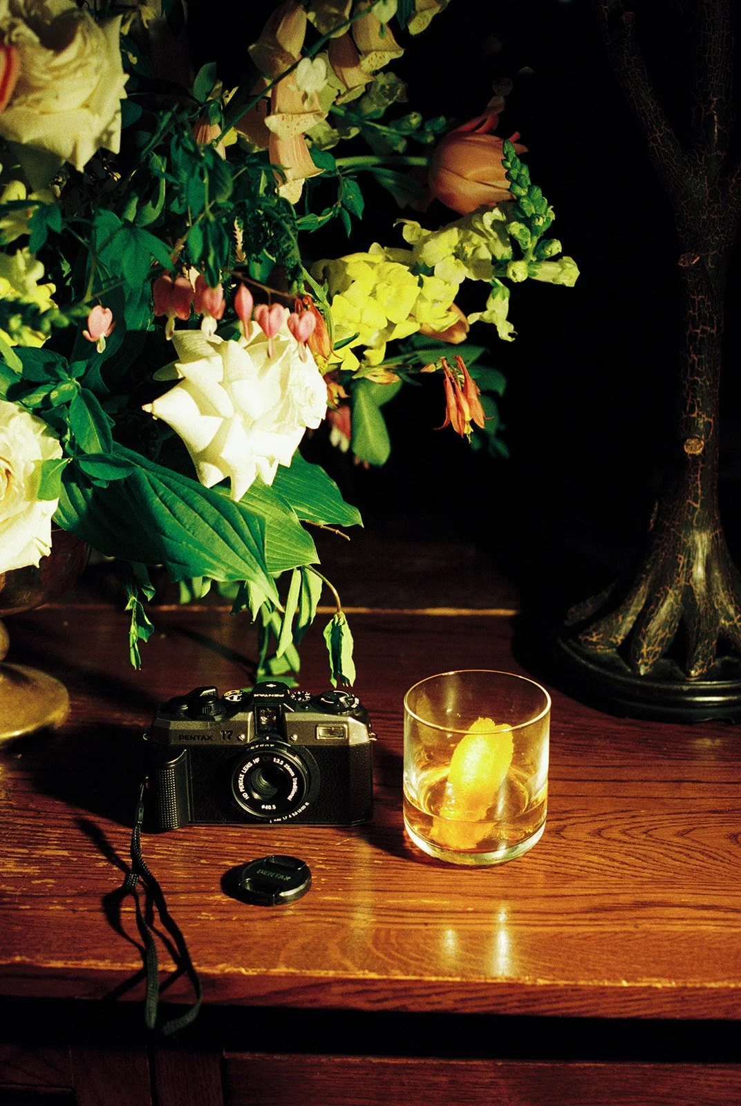 Film wedding detail photo of a vintage Pentax camera, cocktail, and colorful flowers inside Deer Mountain Inn.