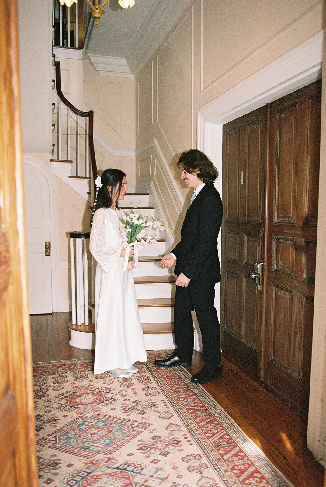 Bride and groom sharing their first look inside Old Town Manor with historic staircase and patterned rug.