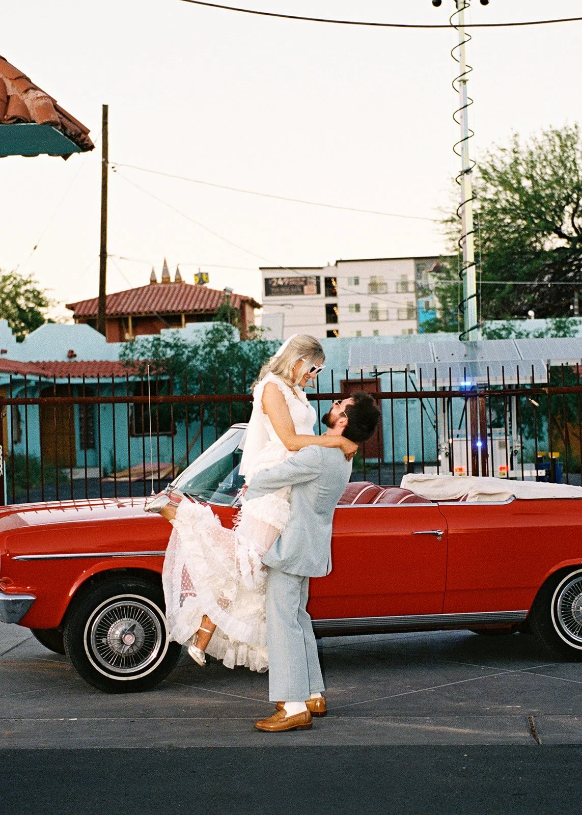 Groom lifting the bride up in front of the red convertible outside of Sure Thing Chapel in Las Vegas.