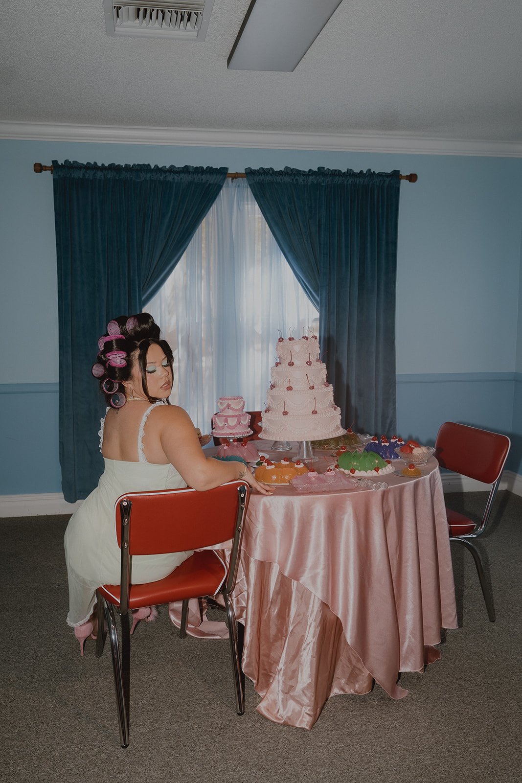 Woman sitting at a vintage dining table with desserts all around her inside The Pink Portal Den in Las Vegas.