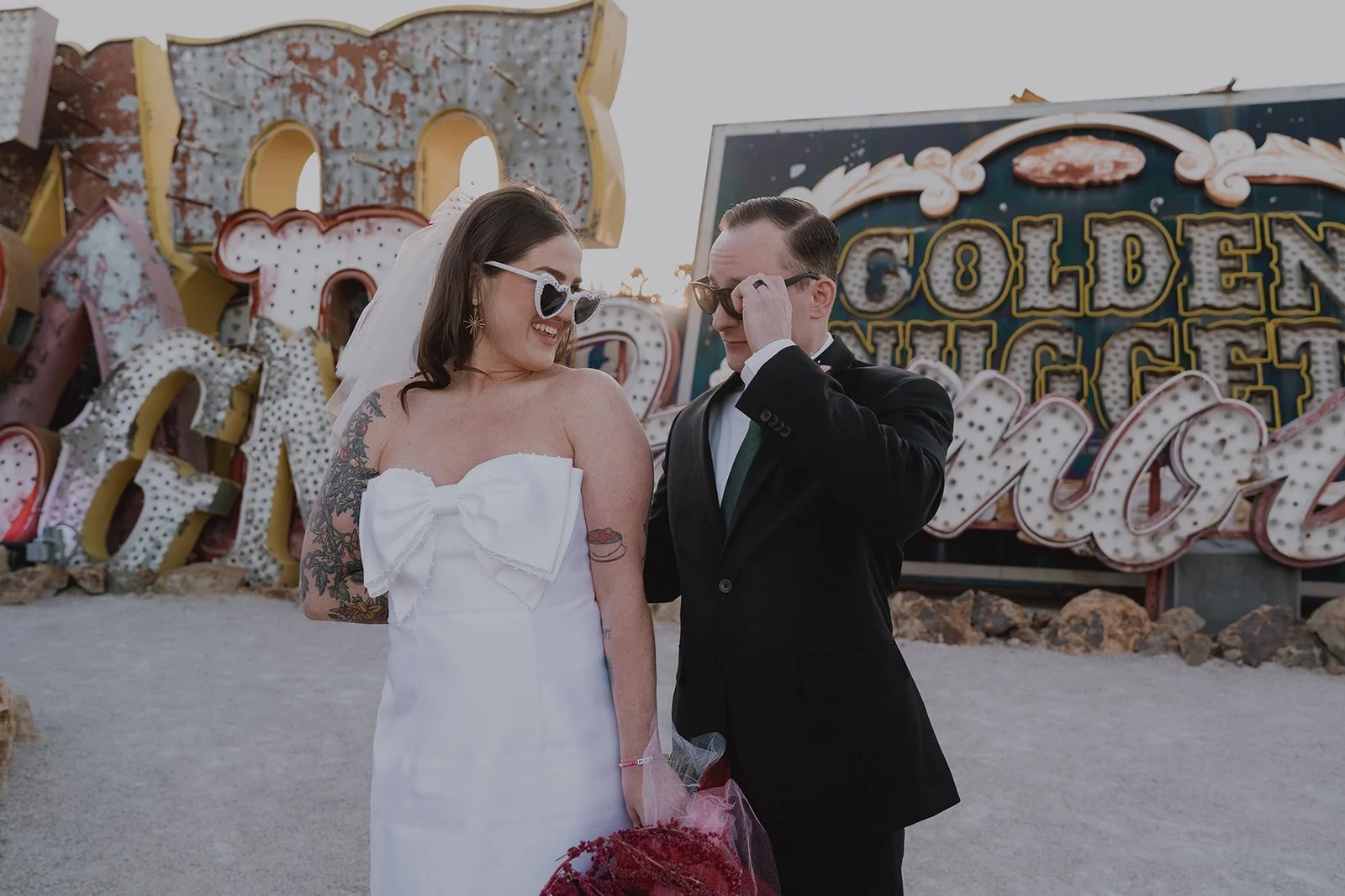 Bride and groom standing together in front of vintage neon signs during golden hour in the North Gallery at the Neon Museum in Las Vegas.
