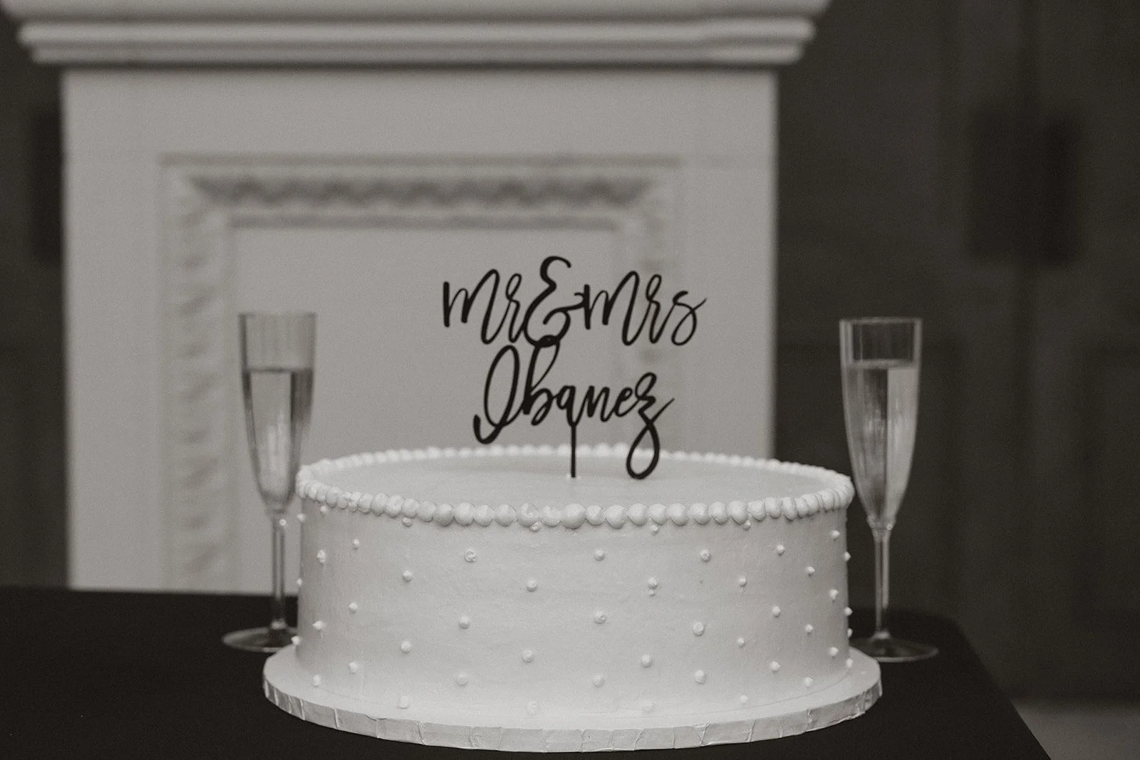 Black and white photo of a wedding cake with “Mr & Mrs” topper and champagne glasses at a Caesars Palace Venus Garden wedding.