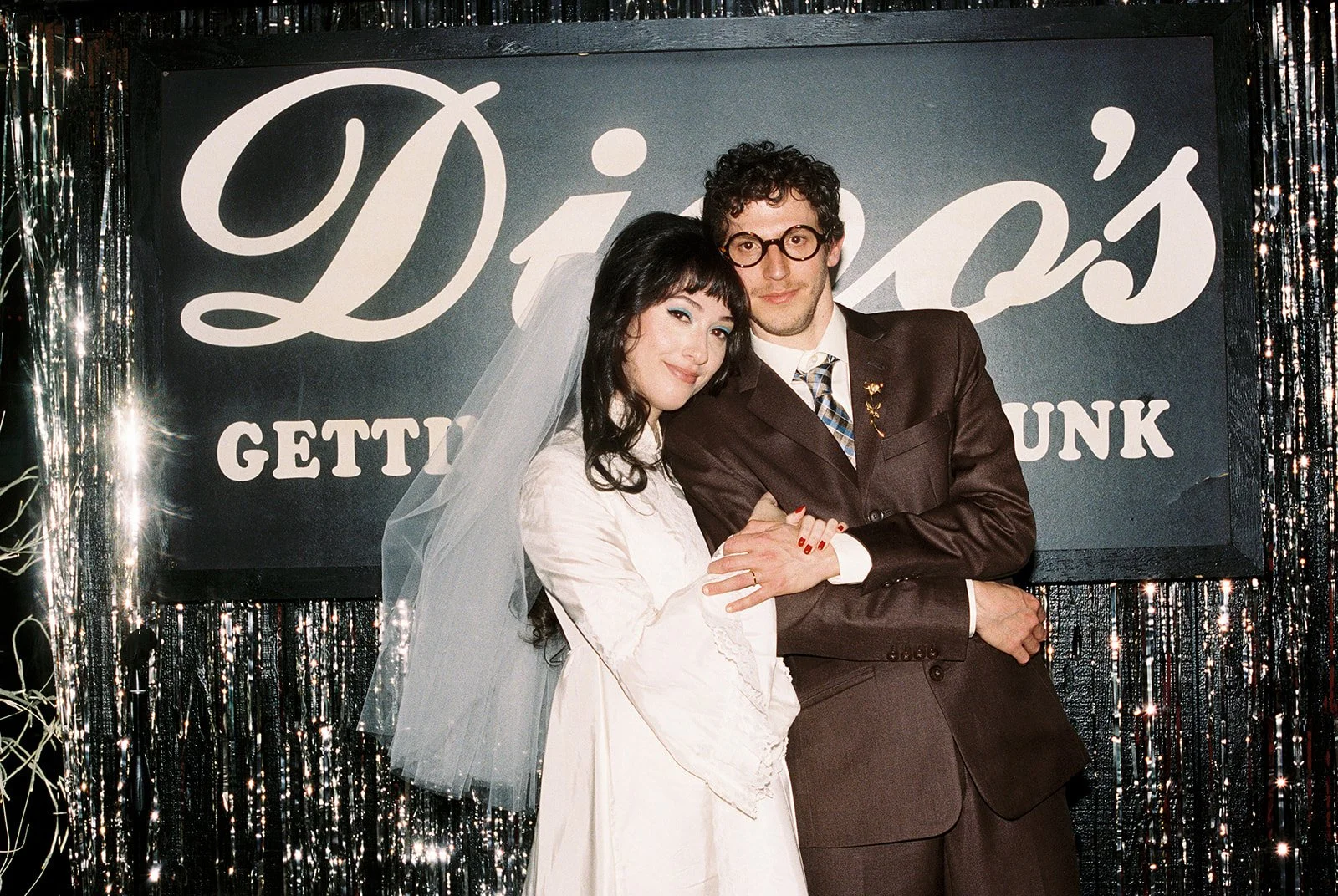 Couple posing in front of a sparkly fringe sign inside Dino's Bar in Las Vegas.