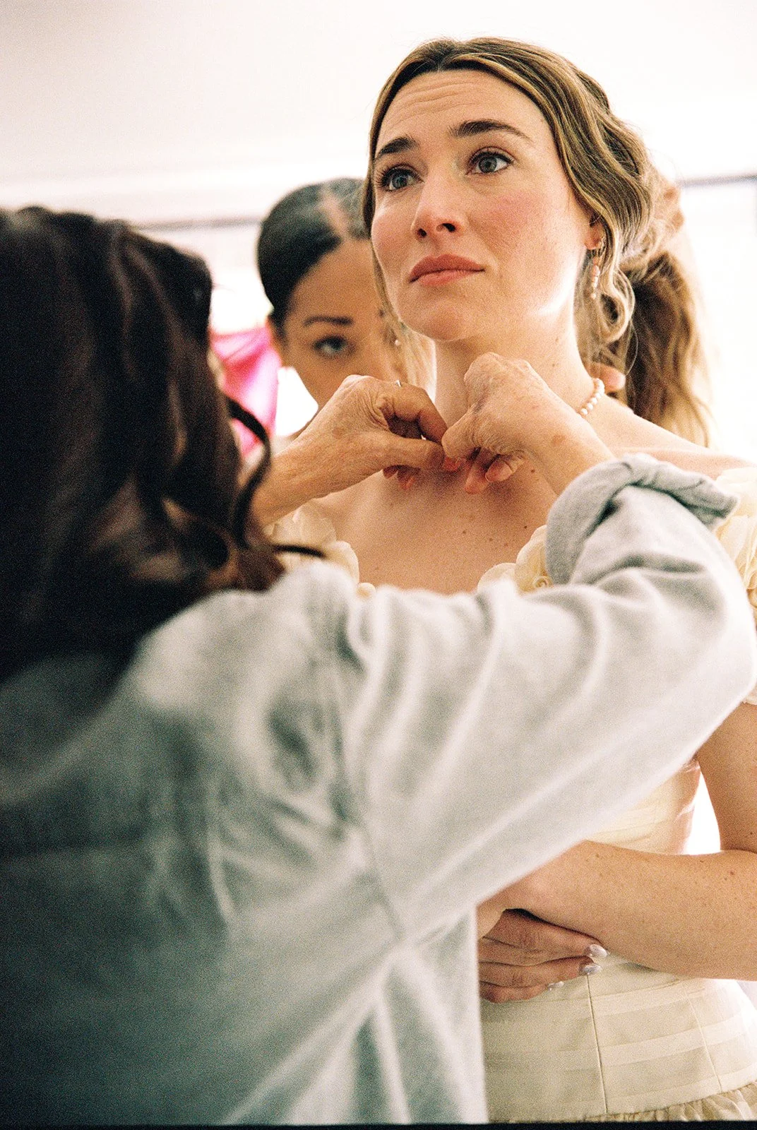 Candid film photo of the bride having her pearl necklace fastened while getting ready for her Catskills wedding.