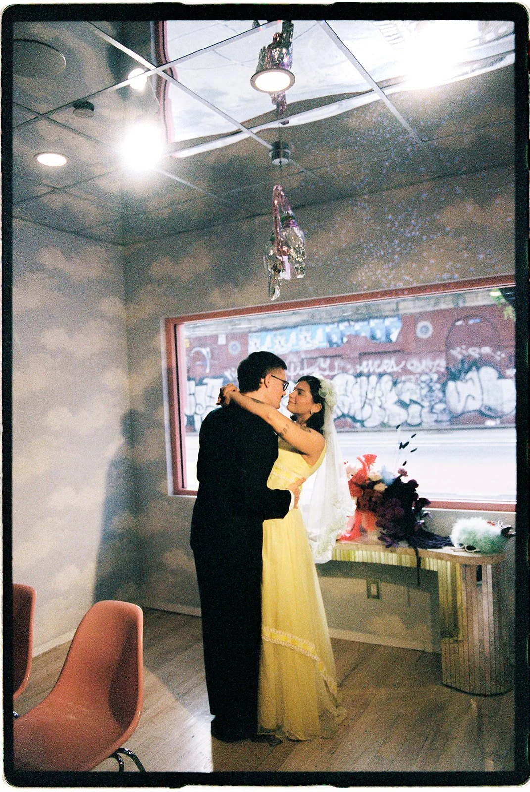Couple embracing inside Sure Thing NYC wedding chapel beside a large window overlooking the Lower East Side.