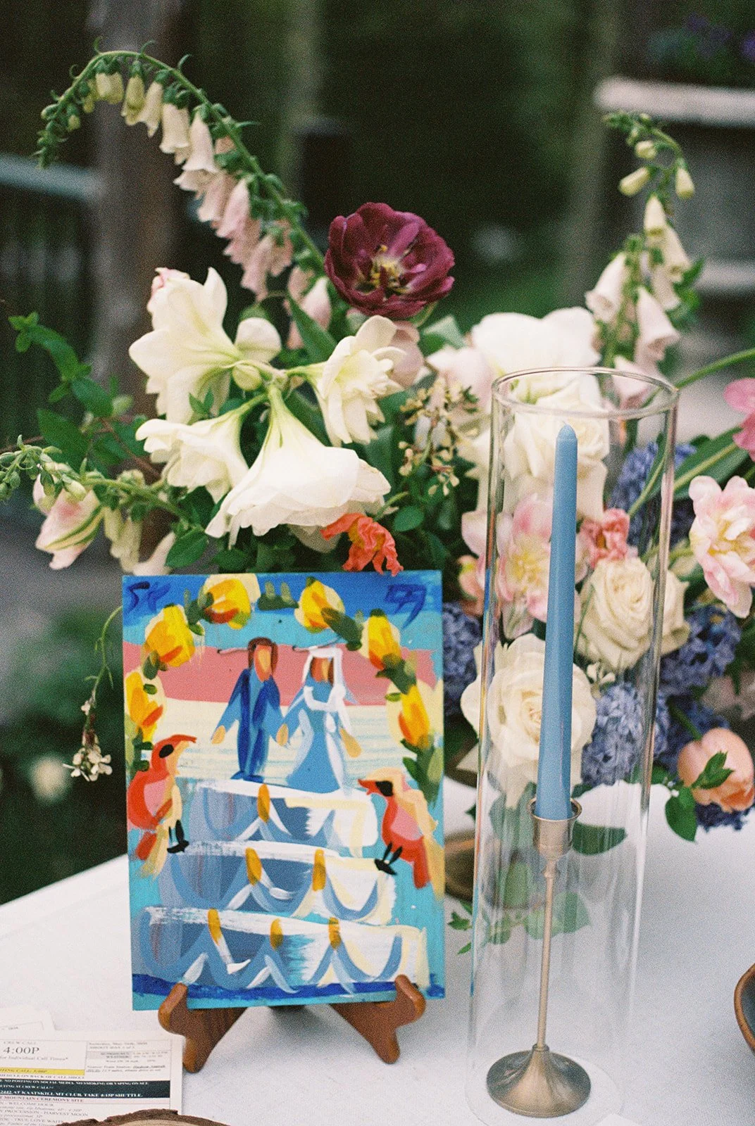 Film wedding detail photo of colorful flowers, a blue taper candle, and a small painted portrait at Deer Mountain Inn.