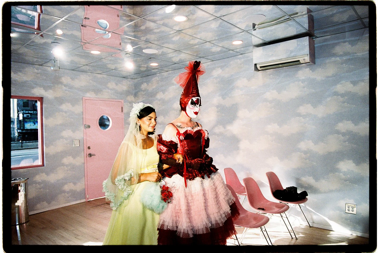 Bride in a pale yellow wedding dress standing arm in arm with Tillie the Clown inside Sure Thing NYC.