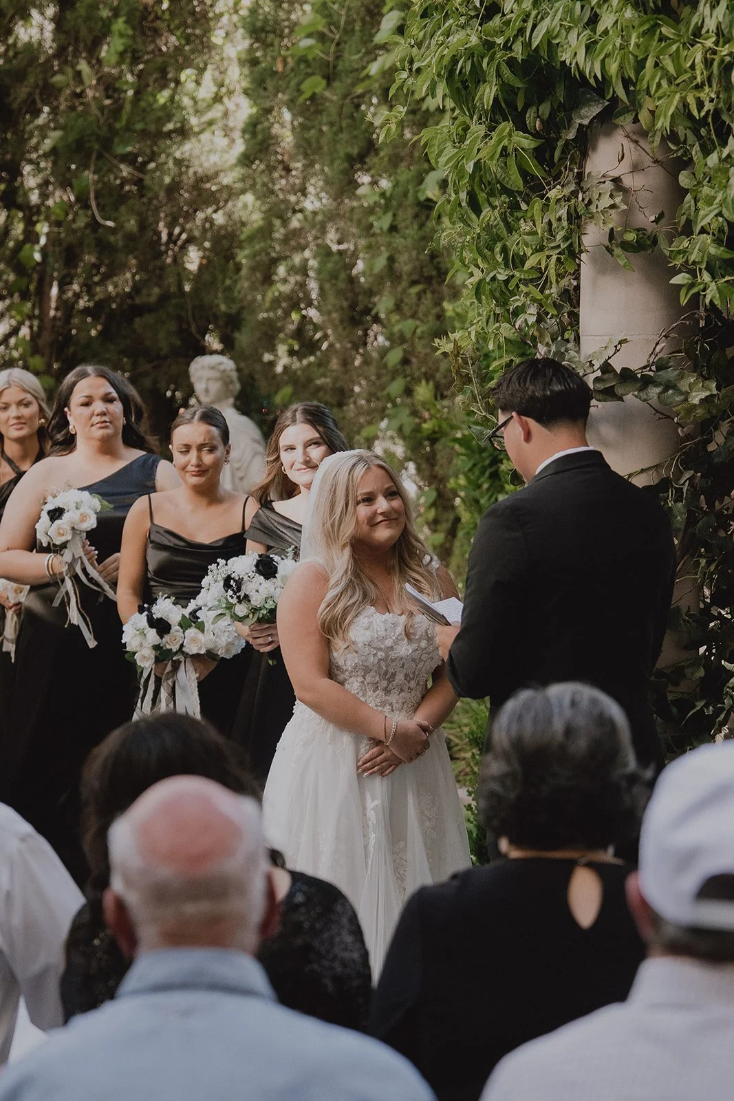 Bride smiling at the groom as he reads his vows during their Caesars Palace Venus Garden wedding ceremony