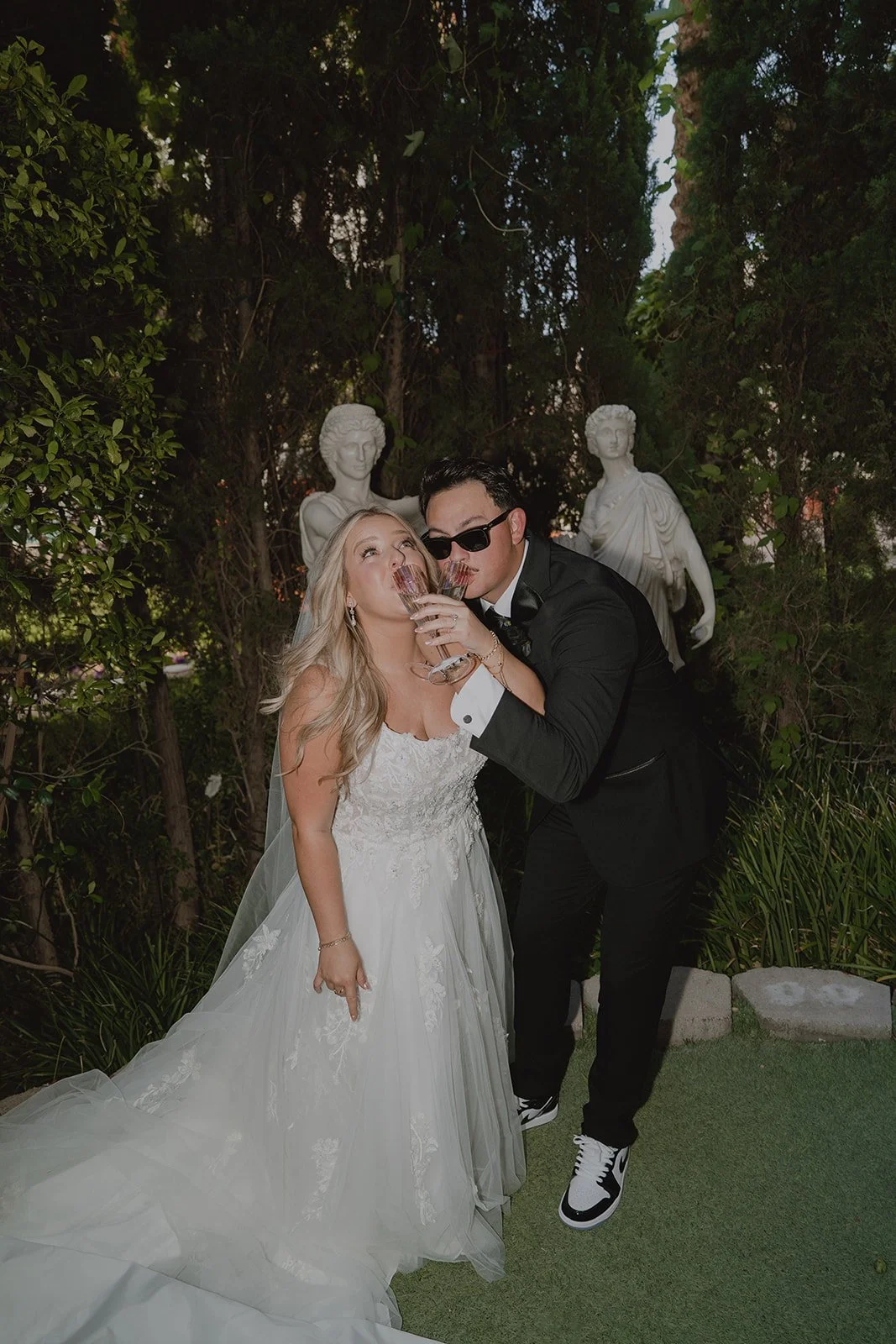 Bride and groom clinking champagne glasses beneath greenery during a micro wedding in Las Vegas.