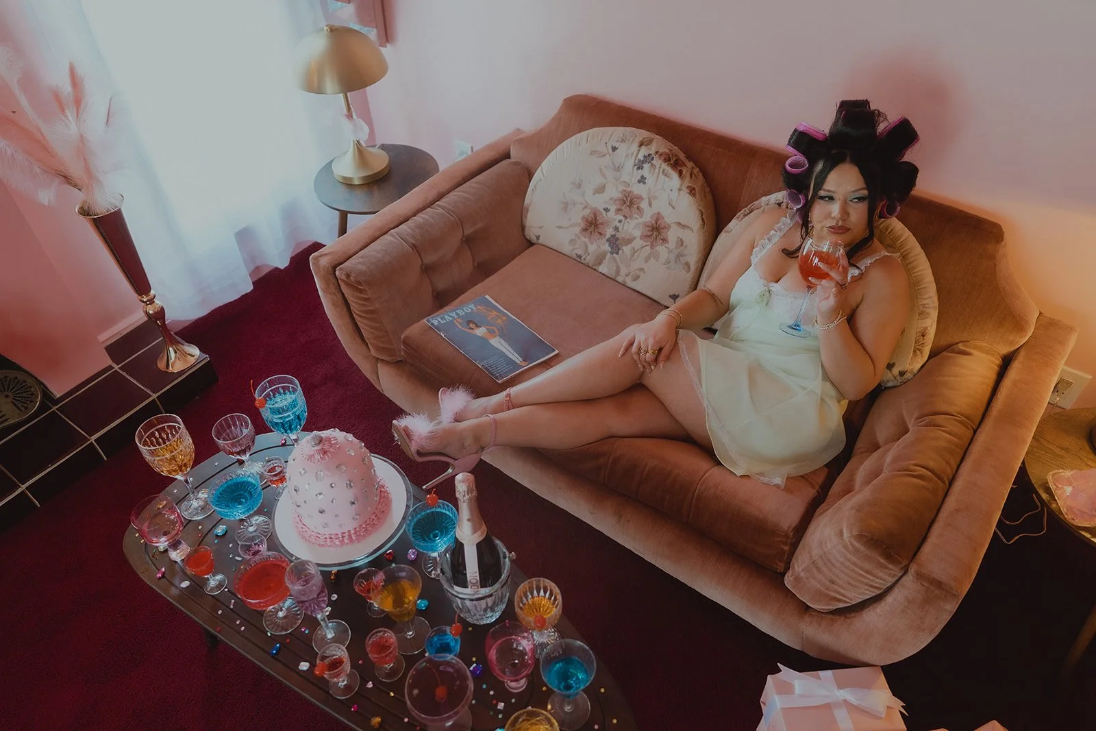 Overhead shot of a woman sitting on a vintage pink couch sipping on a drink in the living room of The Pink Portal Den in Las Vegas.