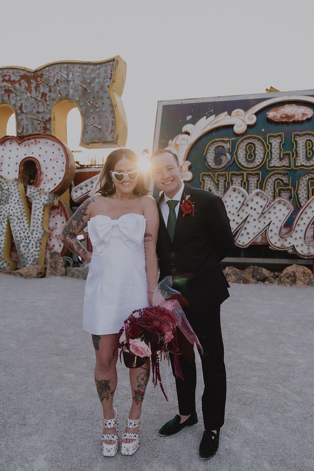 Bride and groom standing together in front of vintage neon signs during golden hour in the North Gallery at the Neon Museum in Las Vegas.