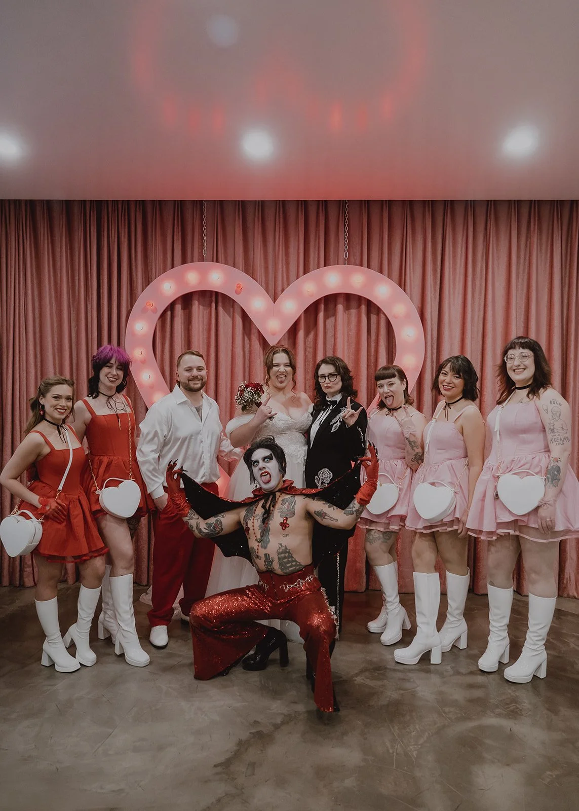 Couple posing with Hellvis and their pink and red wedding party at Sure Thing Chapel.