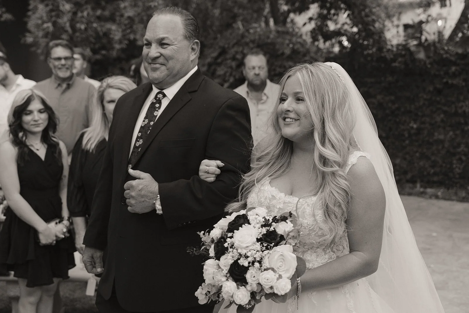 Black and white photo of a bride being walked down the aisle by her father