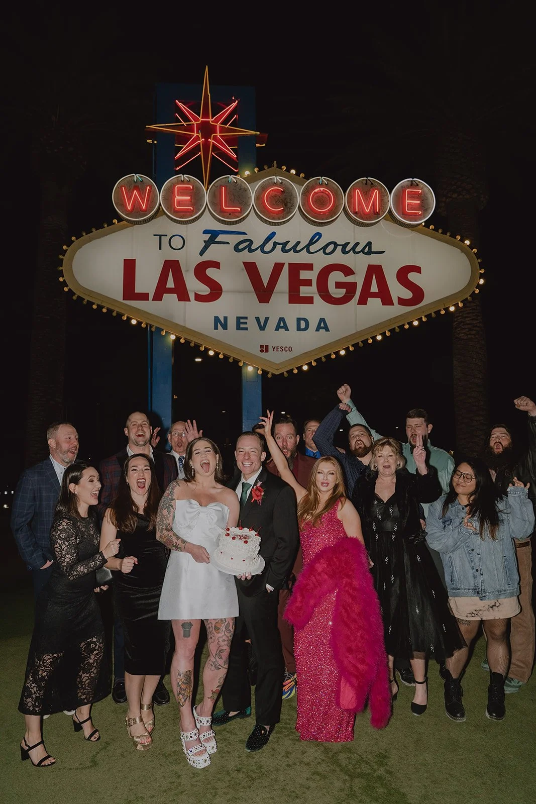 Couple and their guests posing in front of the Welcome to Fabulous Las Vegas sign at night.