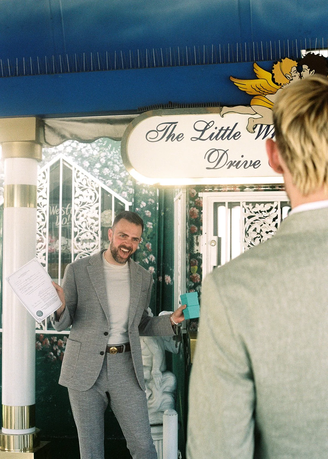 Man stinking out his tongue and holding up his marriage certificate and ring boxes.