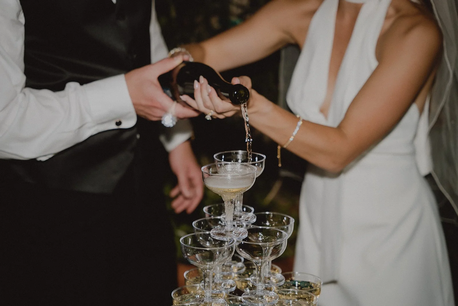 Close up shot of a bride and groom pouring champagne into their champagne tower.