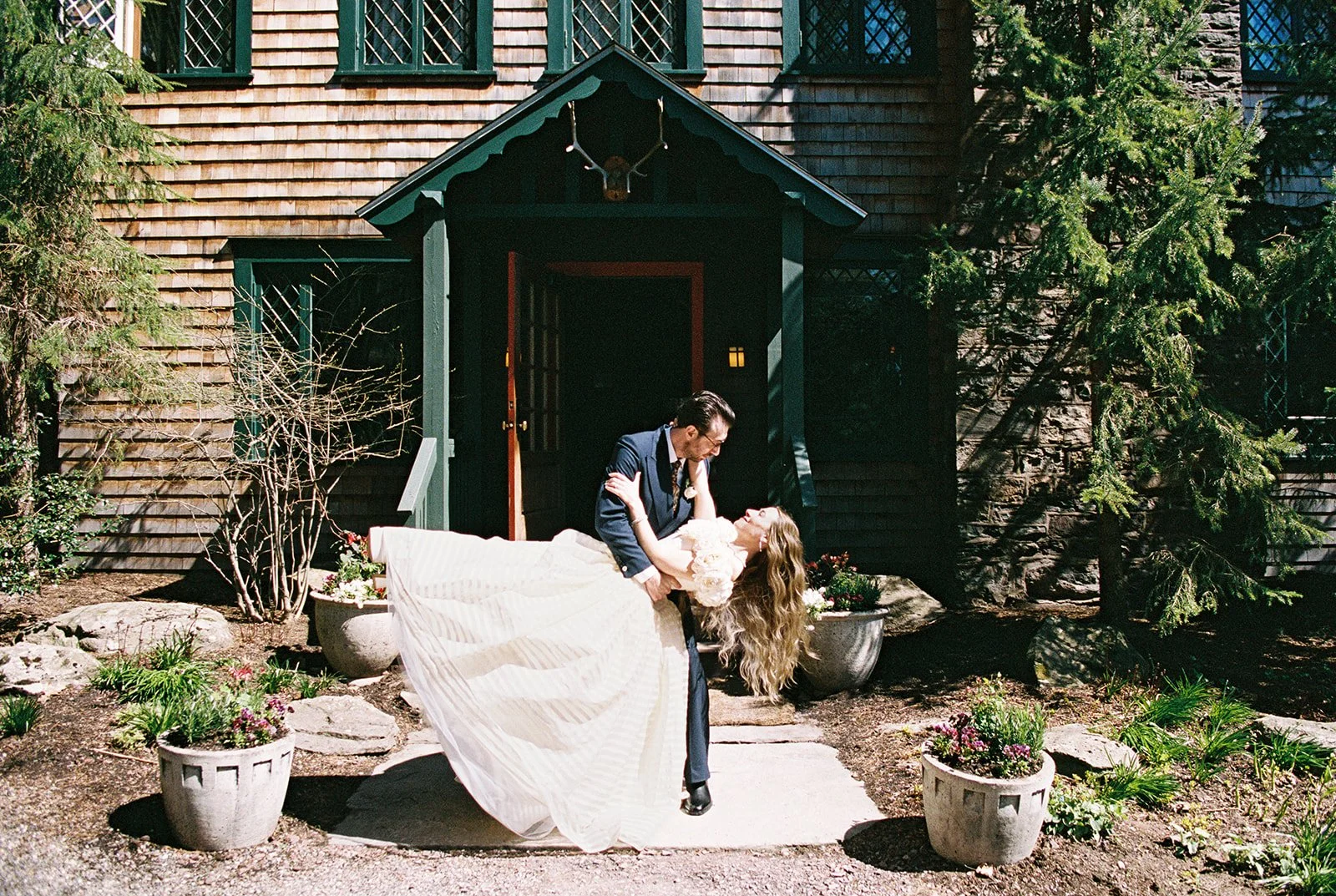Film wedding portrait of the groom dipping the bride in front of the Deer Mountain Inn entrance.