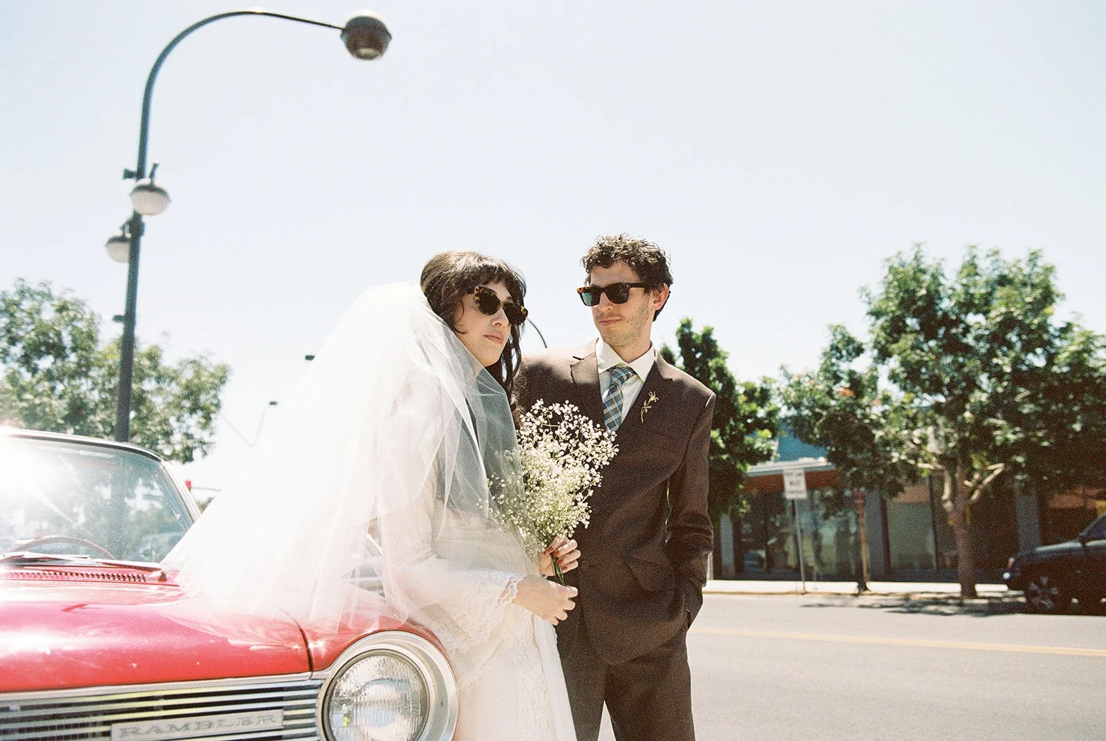 Bride and groom posing with a classic red convertible.