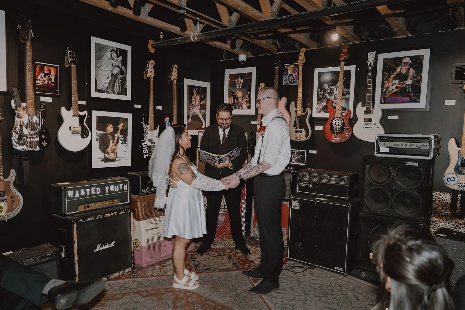 Bride and groom holding hands during their intimate ceremony in the Jam Room at The Punk Rock Museum in Las Vegas.