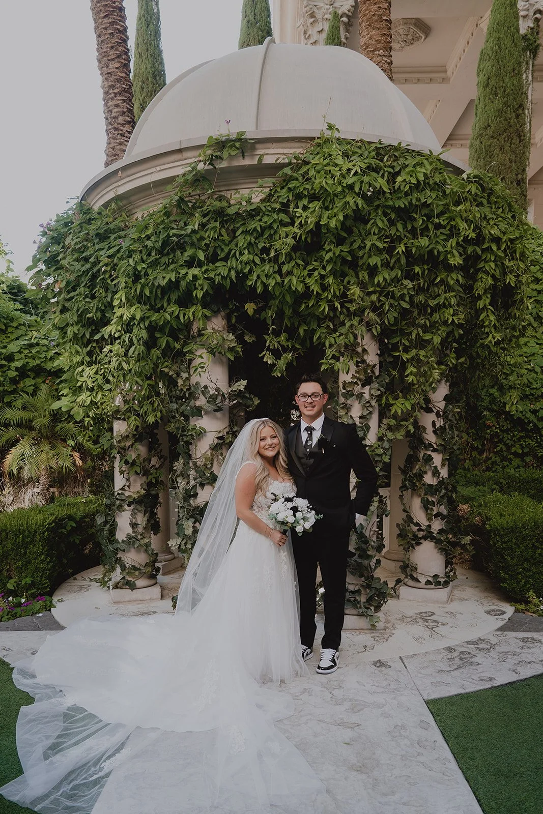 Bride and groom standing together beneath the ivy-covered columns of the Venus Garden at Caesars Palace.