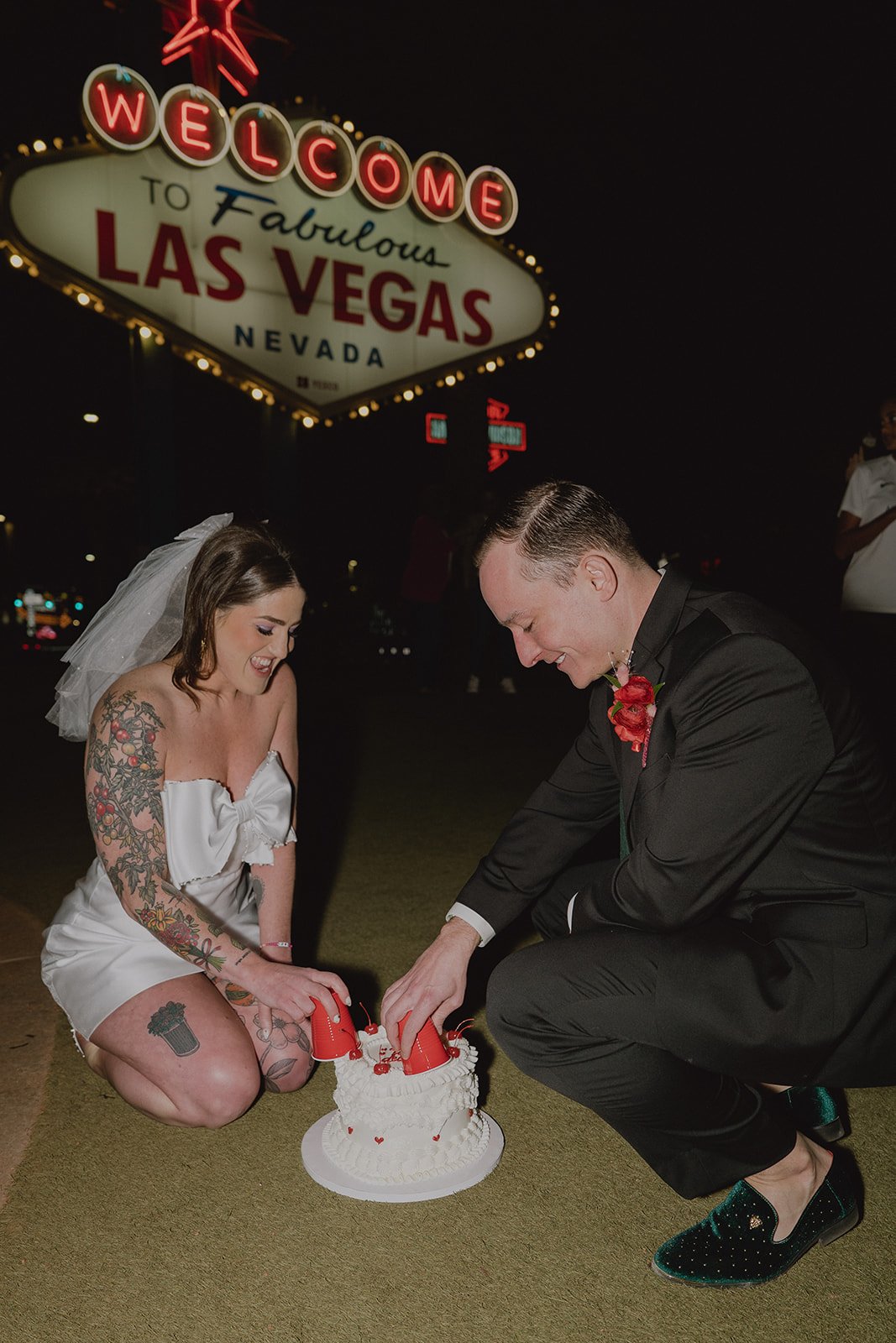 Bride and groom cutting their wedding cake with guests nearby at the Welcome to Fabulous Las Vegas sign.
